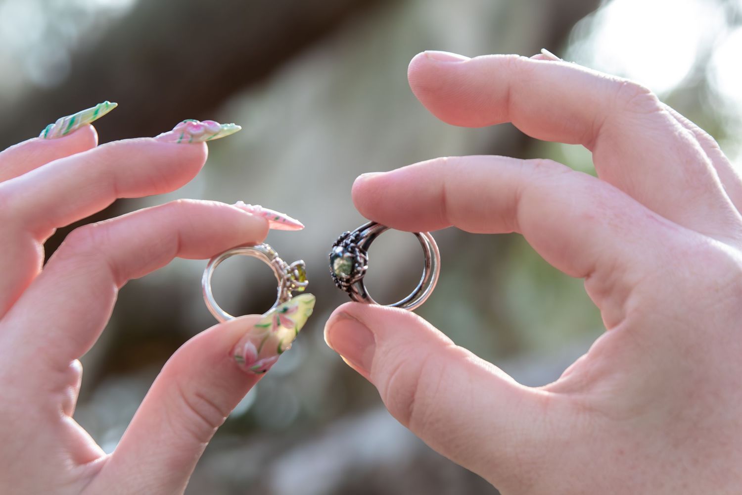 Two hands holding wedding rings with colorful nail art outdoors.