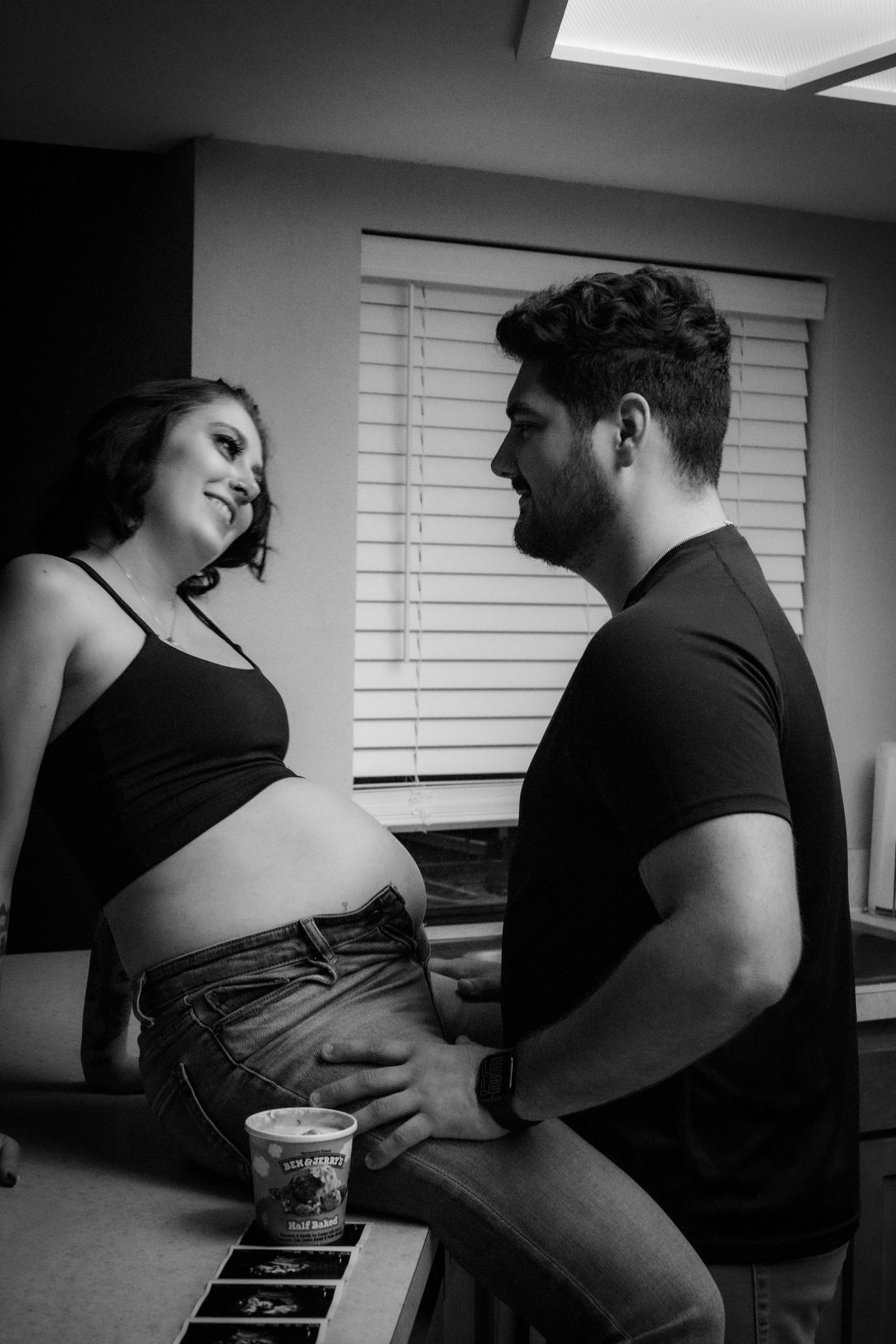Black and white photo of a pregnant woman and man sharing a tender moment together in a home kitchen.