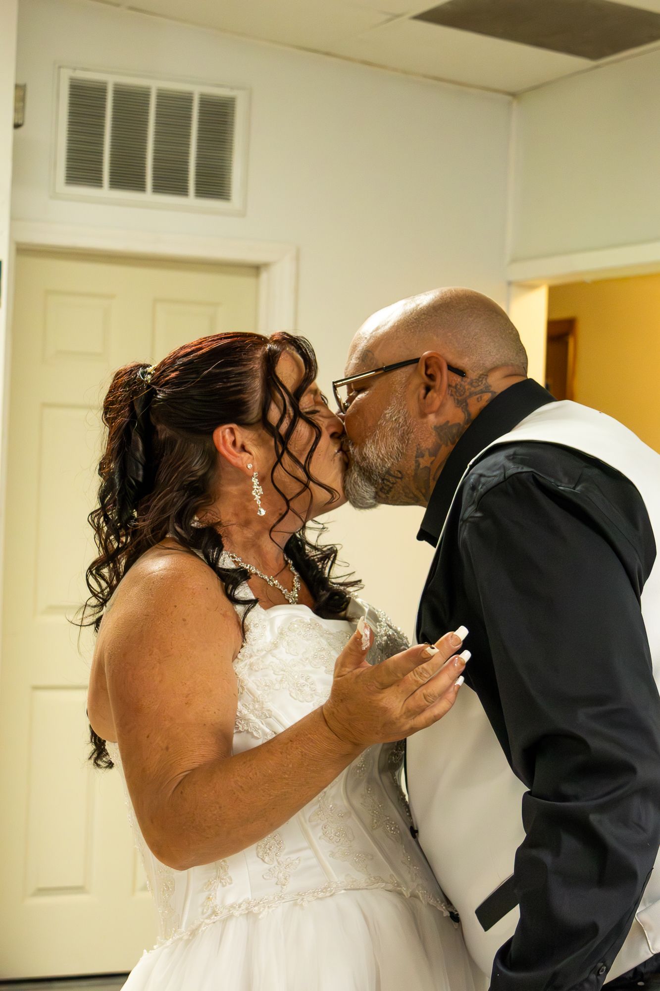 Bride and groom sharing first kiss in white wedding attire during intimate wedding celebration.