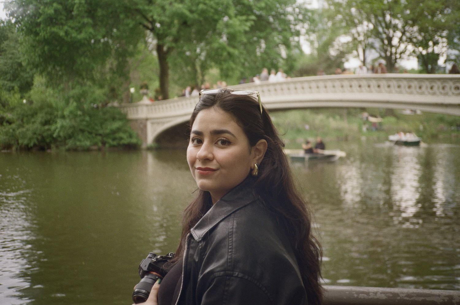 Person sitting by lake in Central Park with bridge and trees in background.