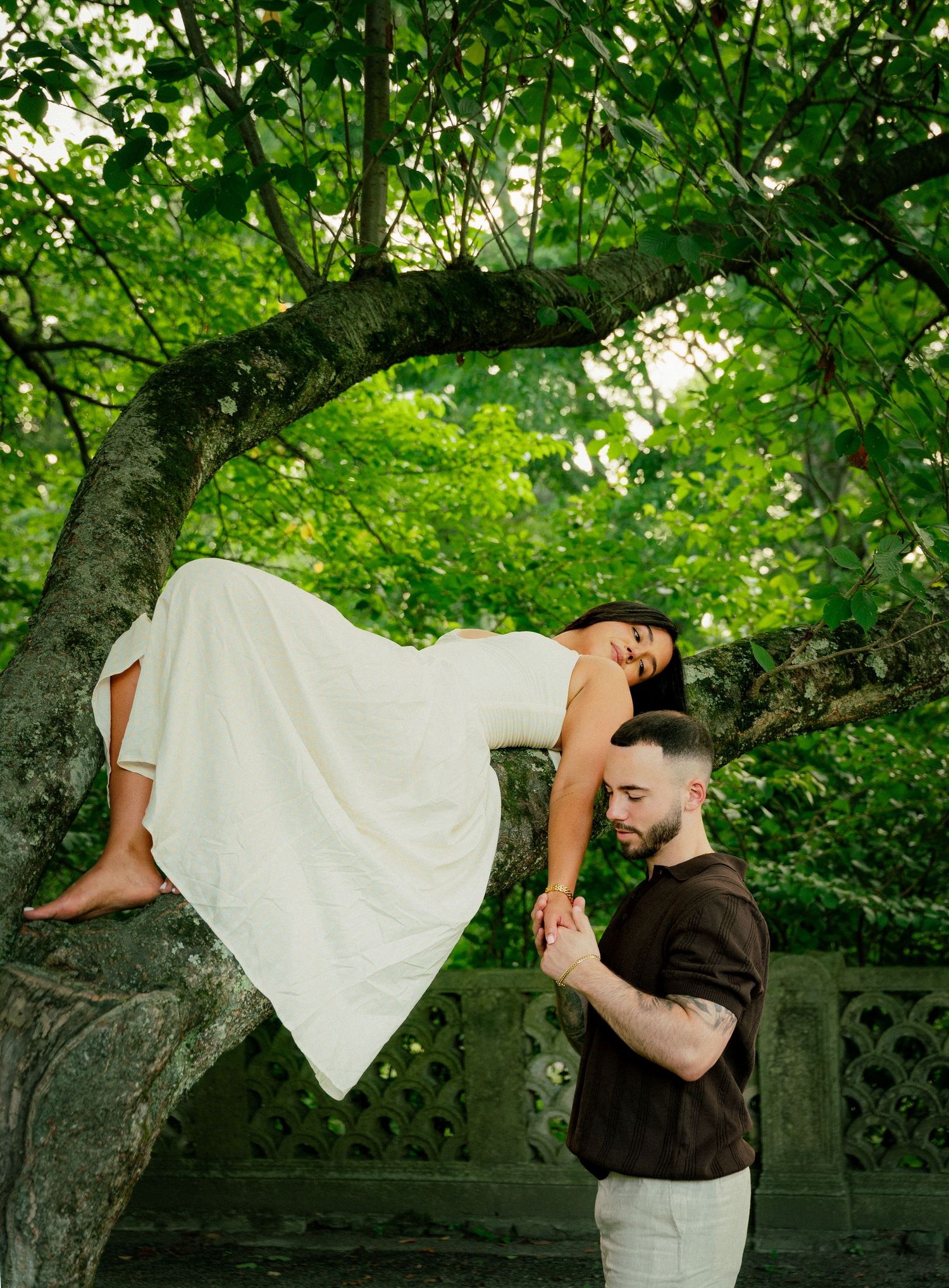 A creative dance pose captured under lush green trees in a garden setting.