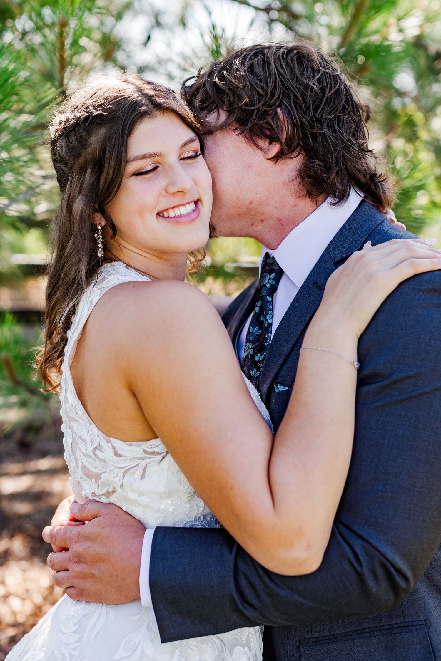 A romantic wedding couple embraces outdoors in a garden setting with natural lighting and greenery.
