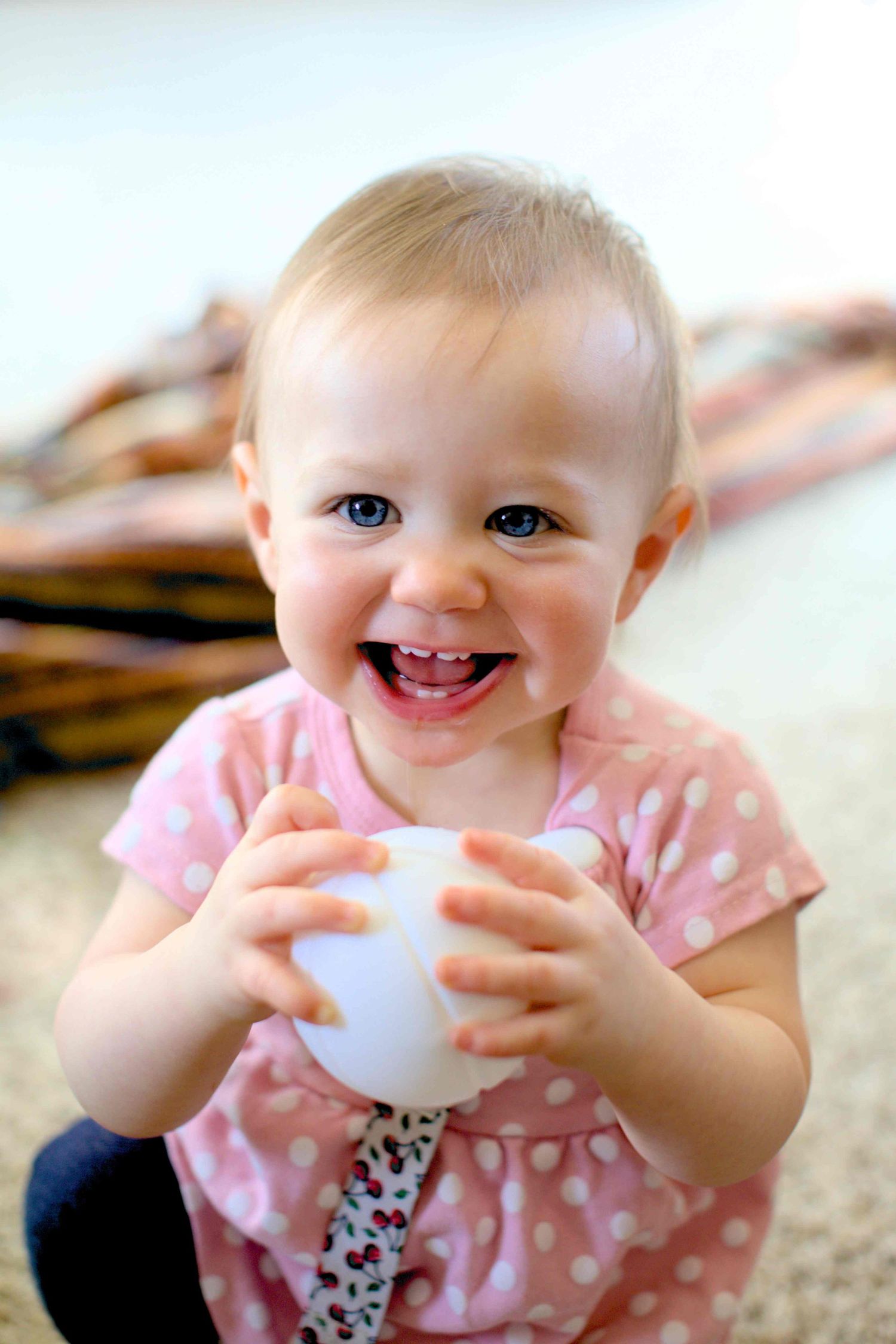 Baby in pink polka dot dress plays with toy on carpet.