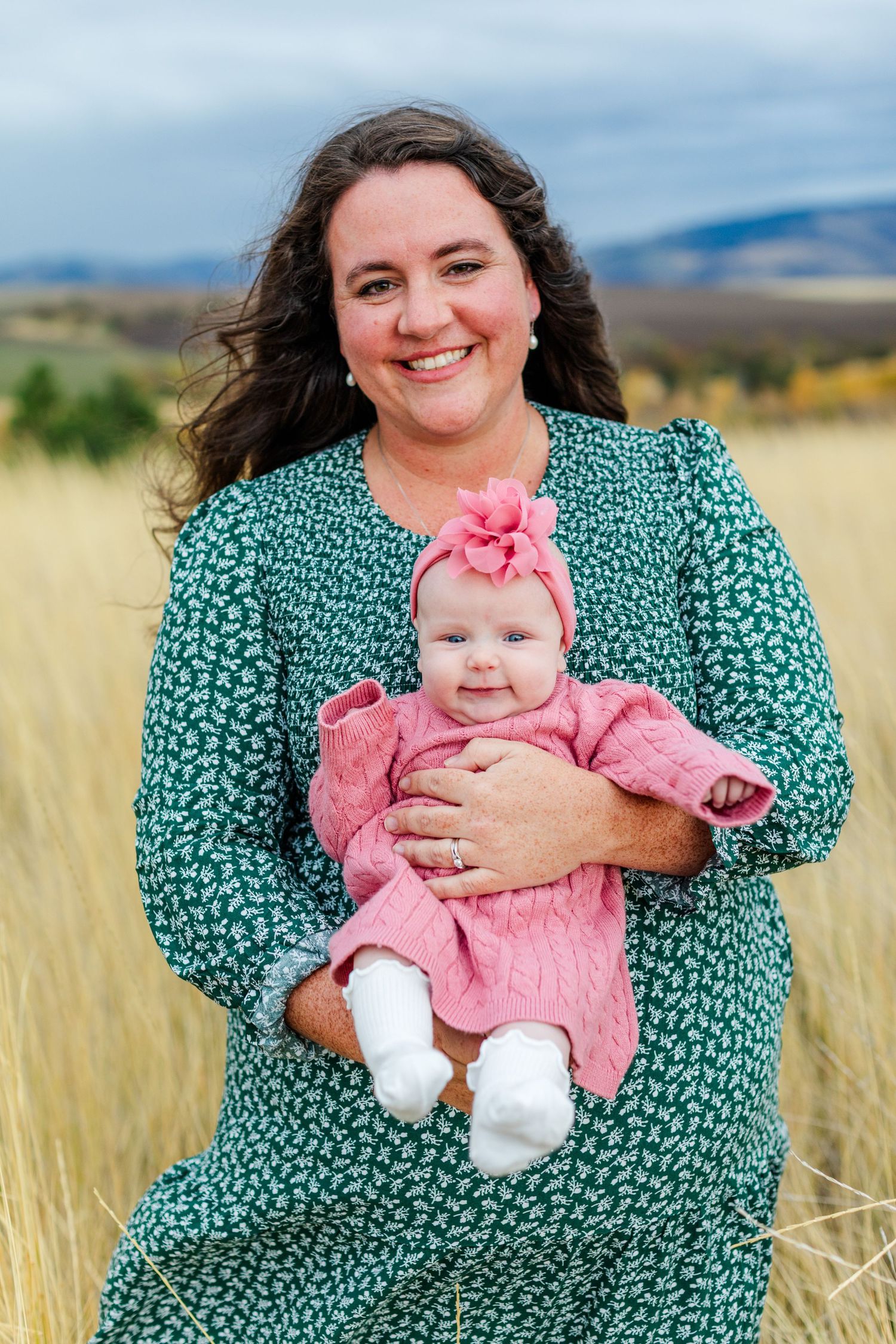 A green floral dress stands out against golden grass in an outdoor family portrait setting.