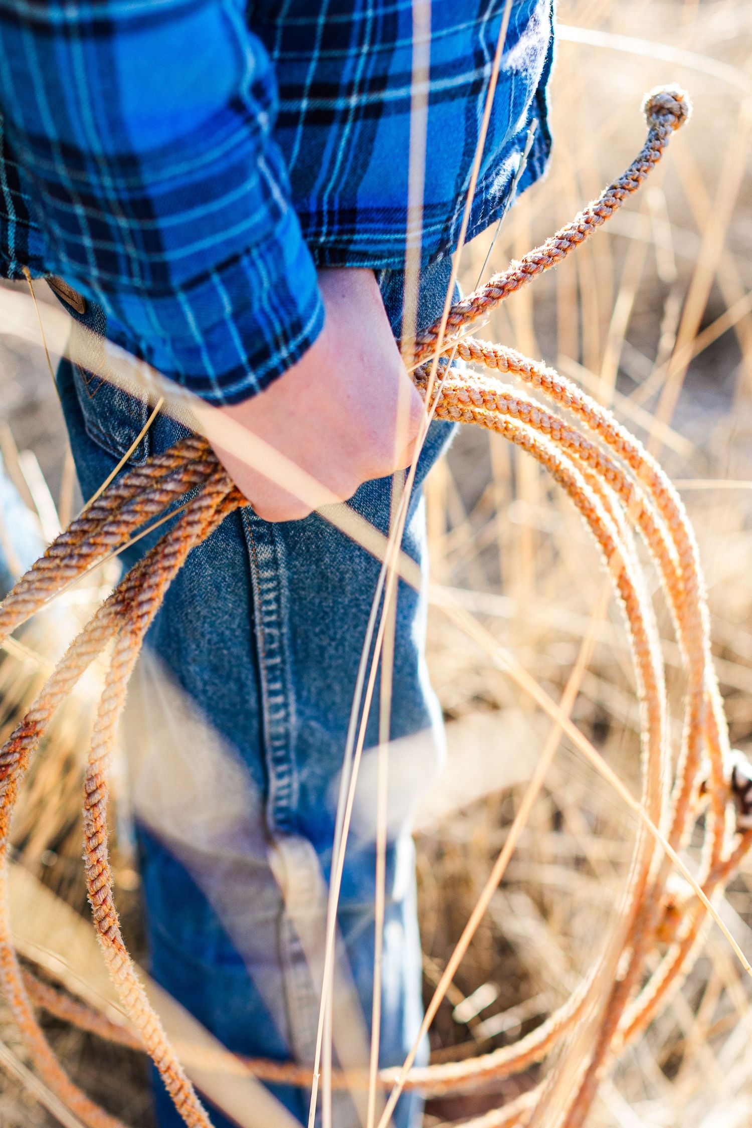 Close-up detail of western rope handling technique with blue plaid shirt and denim jeans.