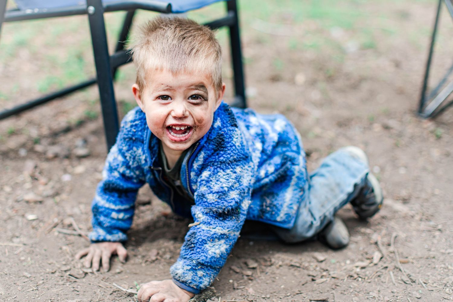 Child in blue patterned outfit playing in dirt outdoors.
