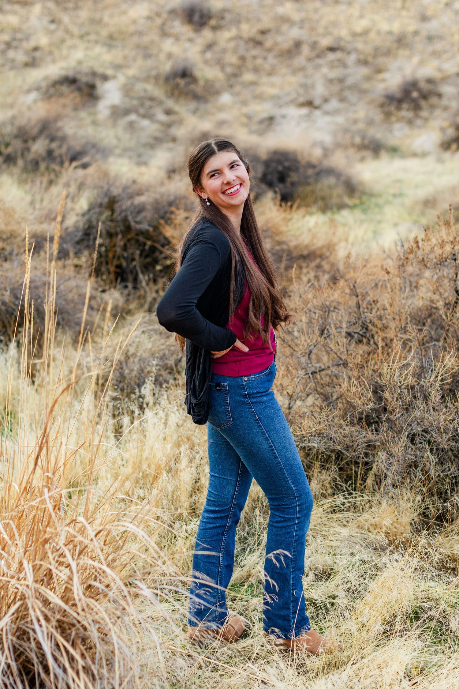 Woman in casual western wear poses playfully in tall autumn grass.