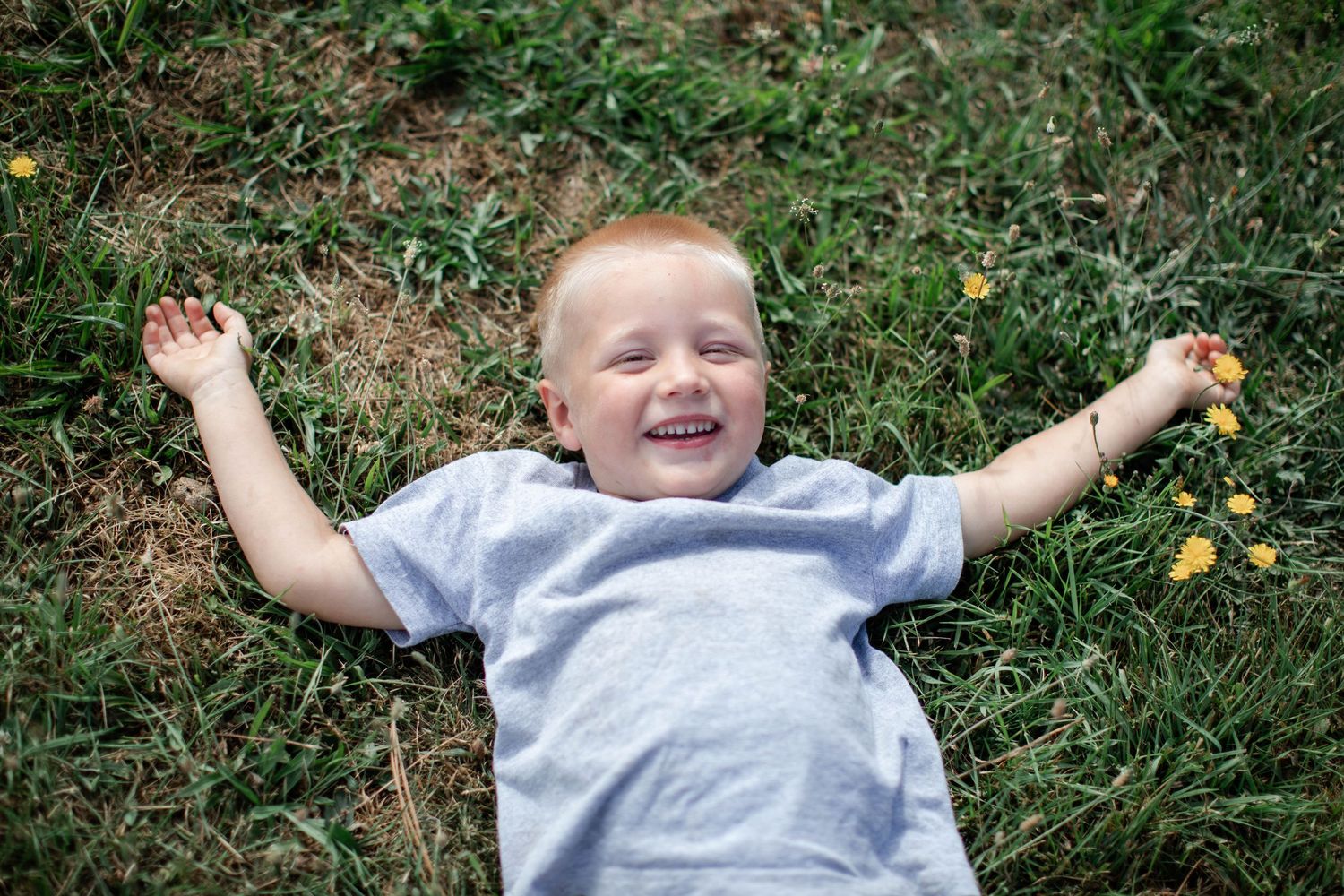 Child lying on grass with arms spread wide, expressing joy outdoors.