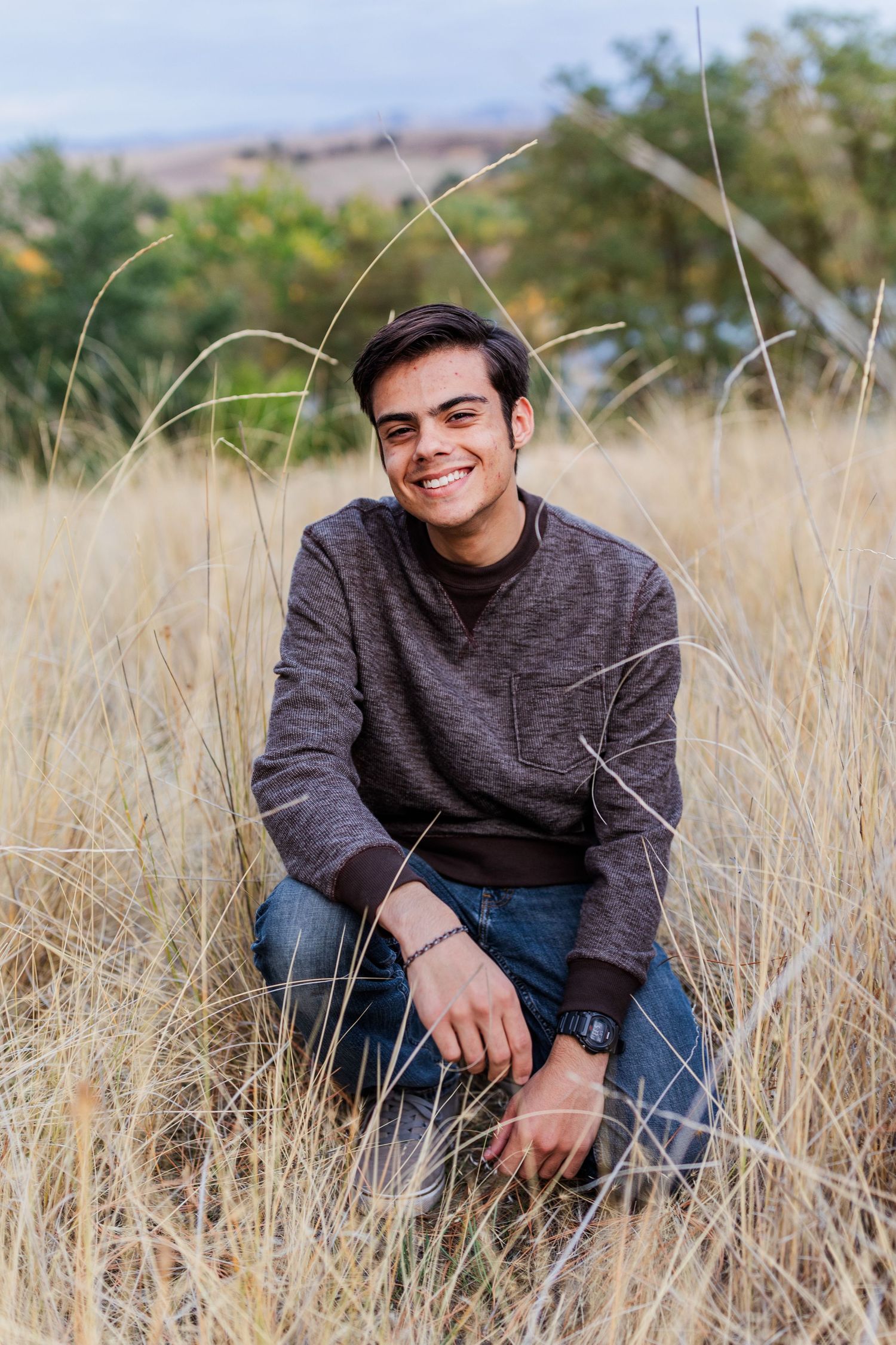 Person in casual wear sits in tall golden grass during autumn.