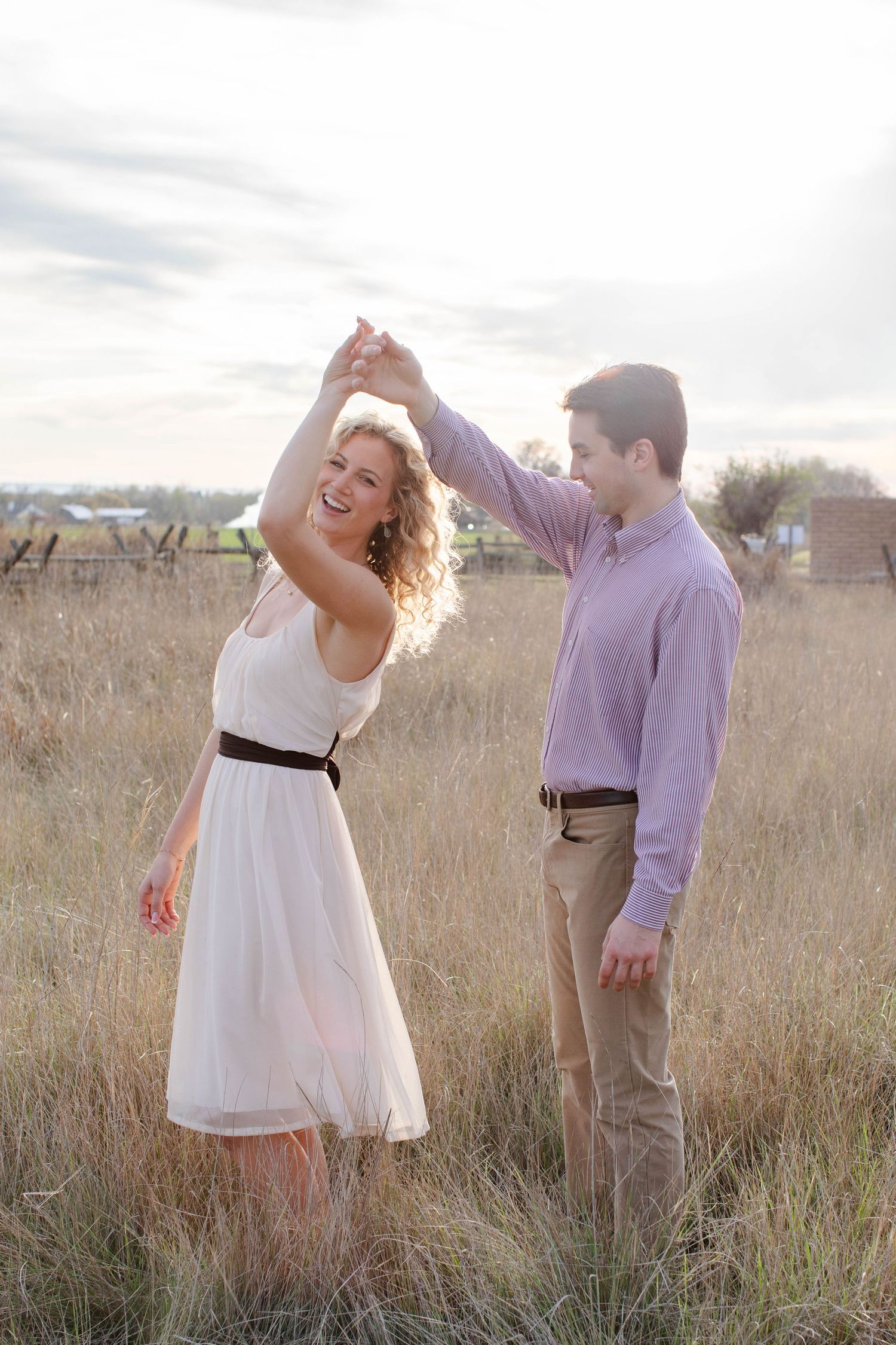 A joyful couple dancing in a golden field, the woman in a white dress laughing as the man spins her at sunset.
