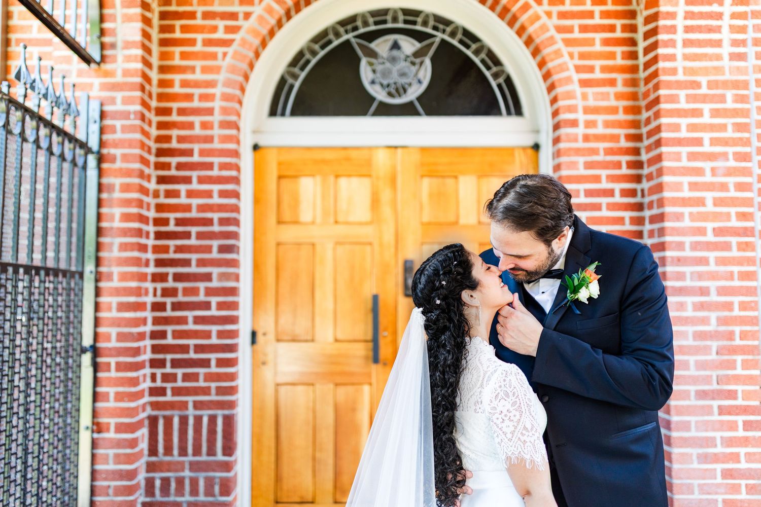 Newlyweds sharing a romantic moment in front of a brick building with an orange door.