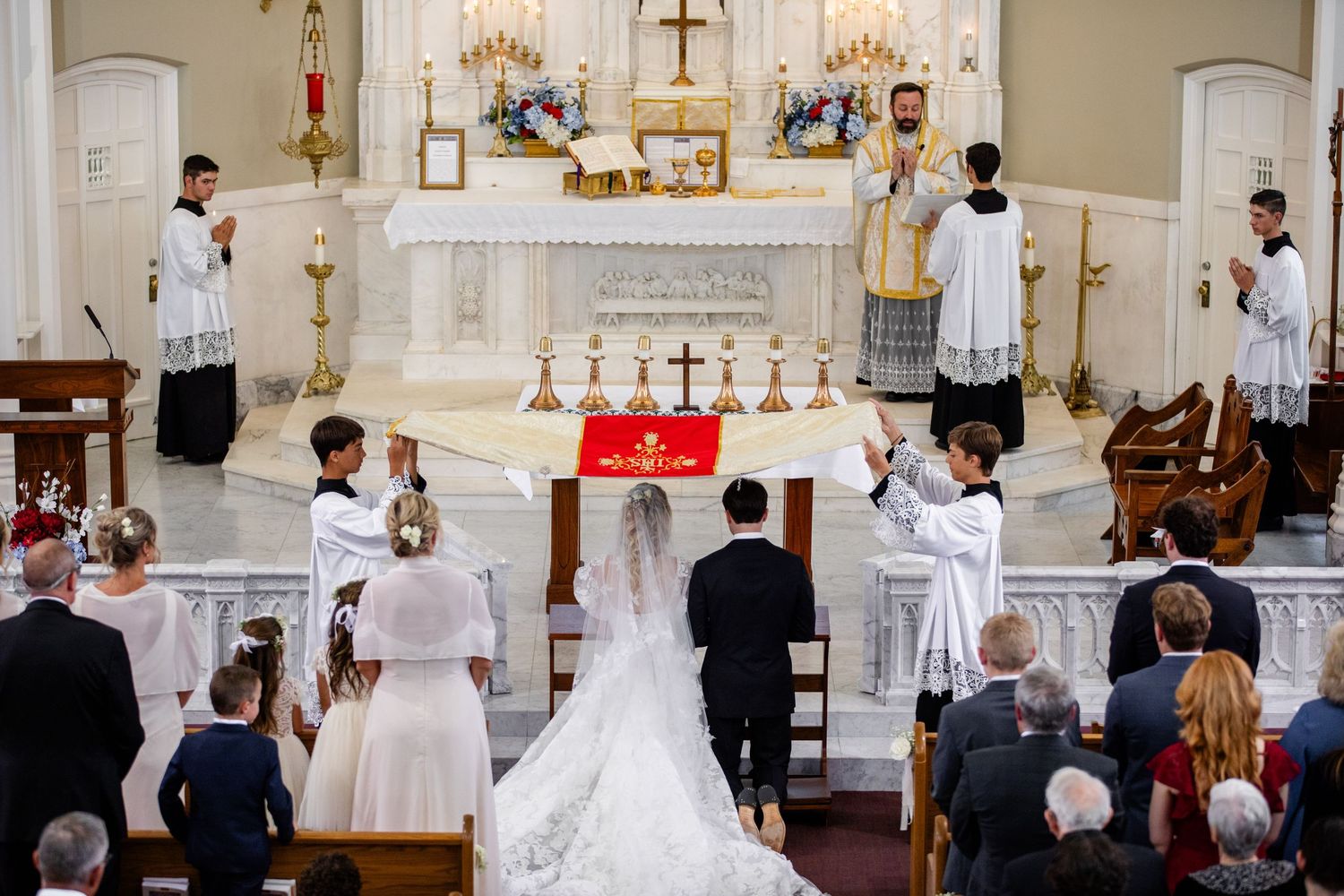 A bride and groom exchange vows at a traditional Catholic church wedding ceremony with altar servers and priest.