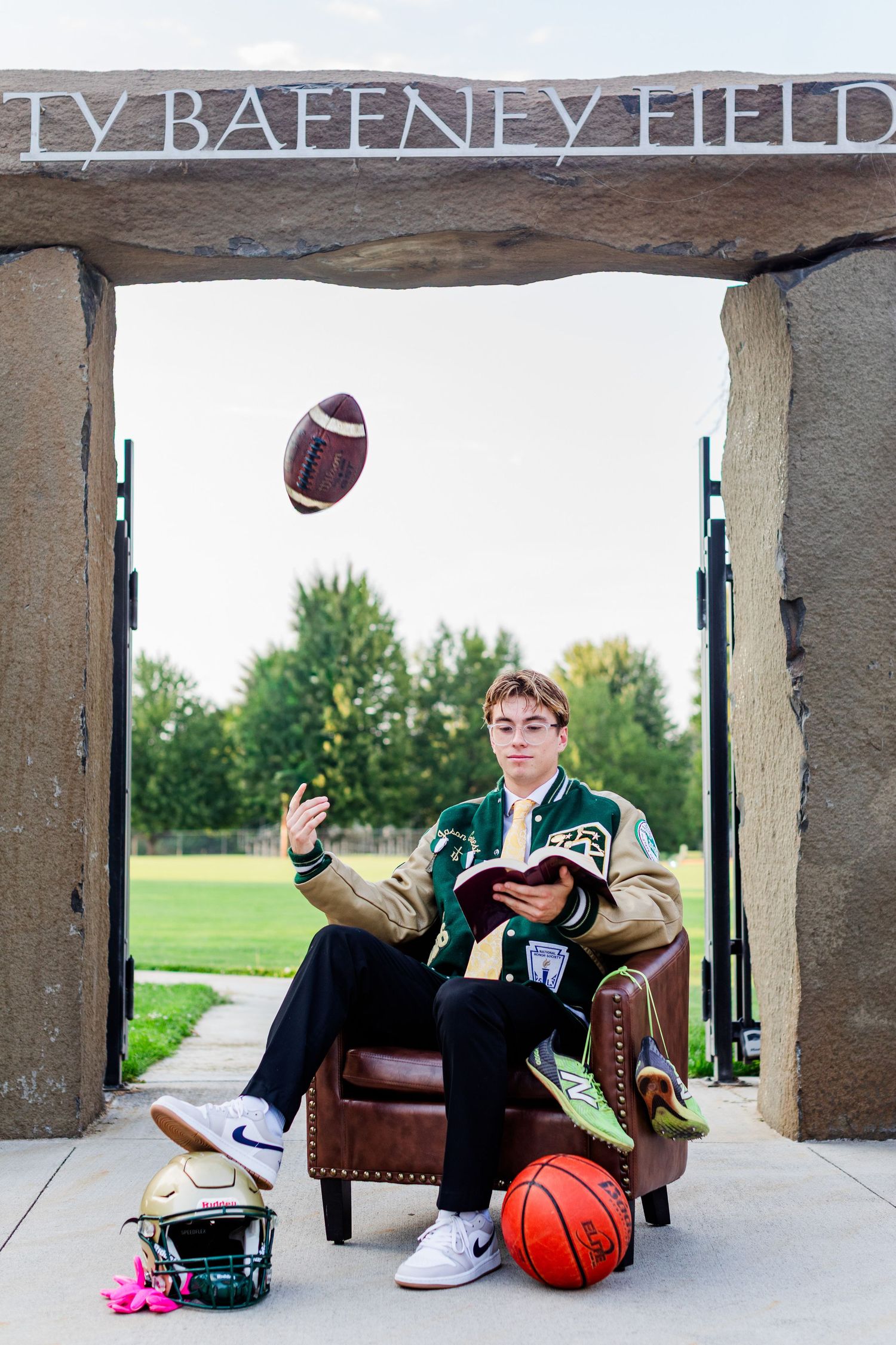 High school athlete poses with sports equipment under stadium entrance for senior portrait.