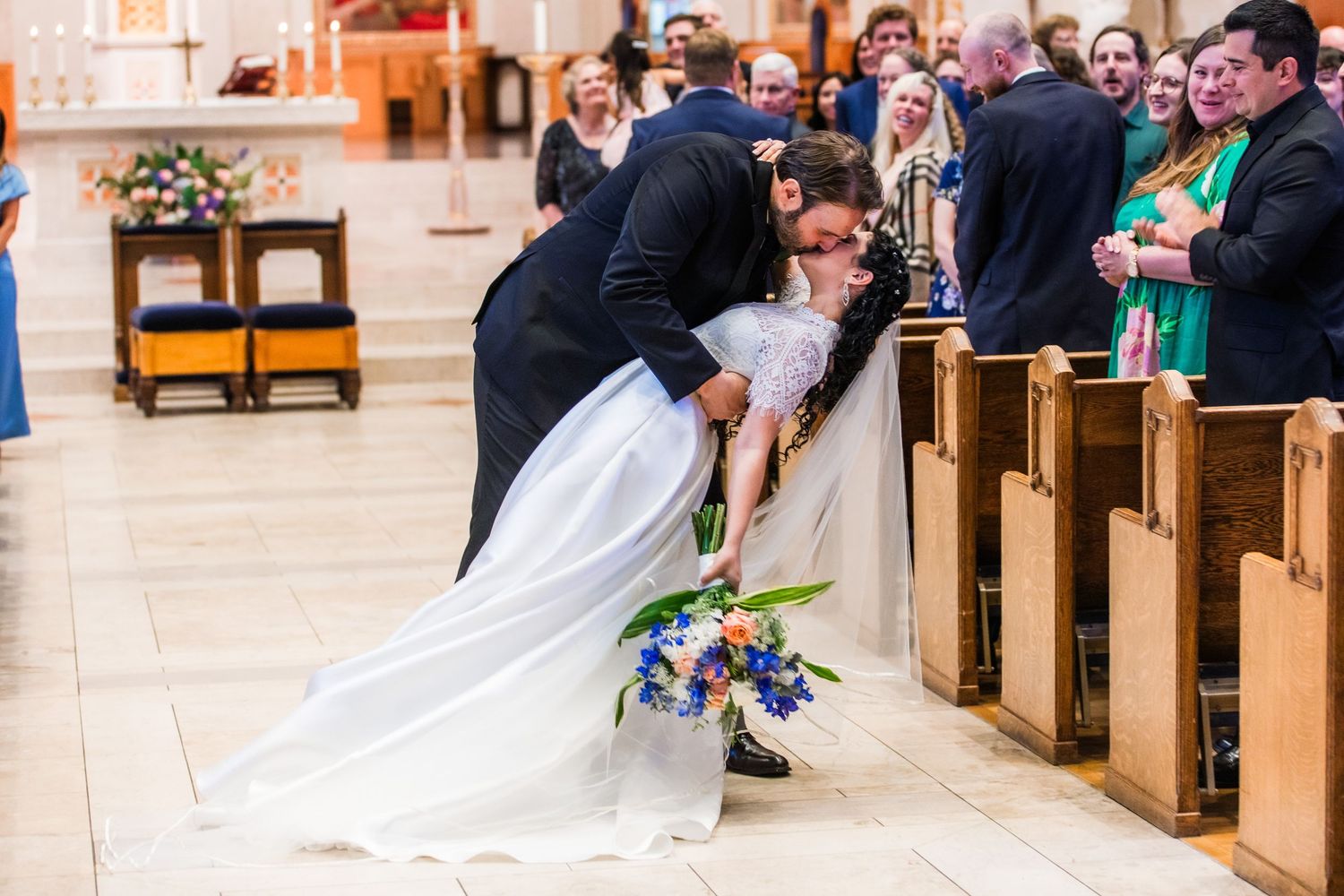 Wedding couple sharing a playful dip in the church aisle surrounded by guests.