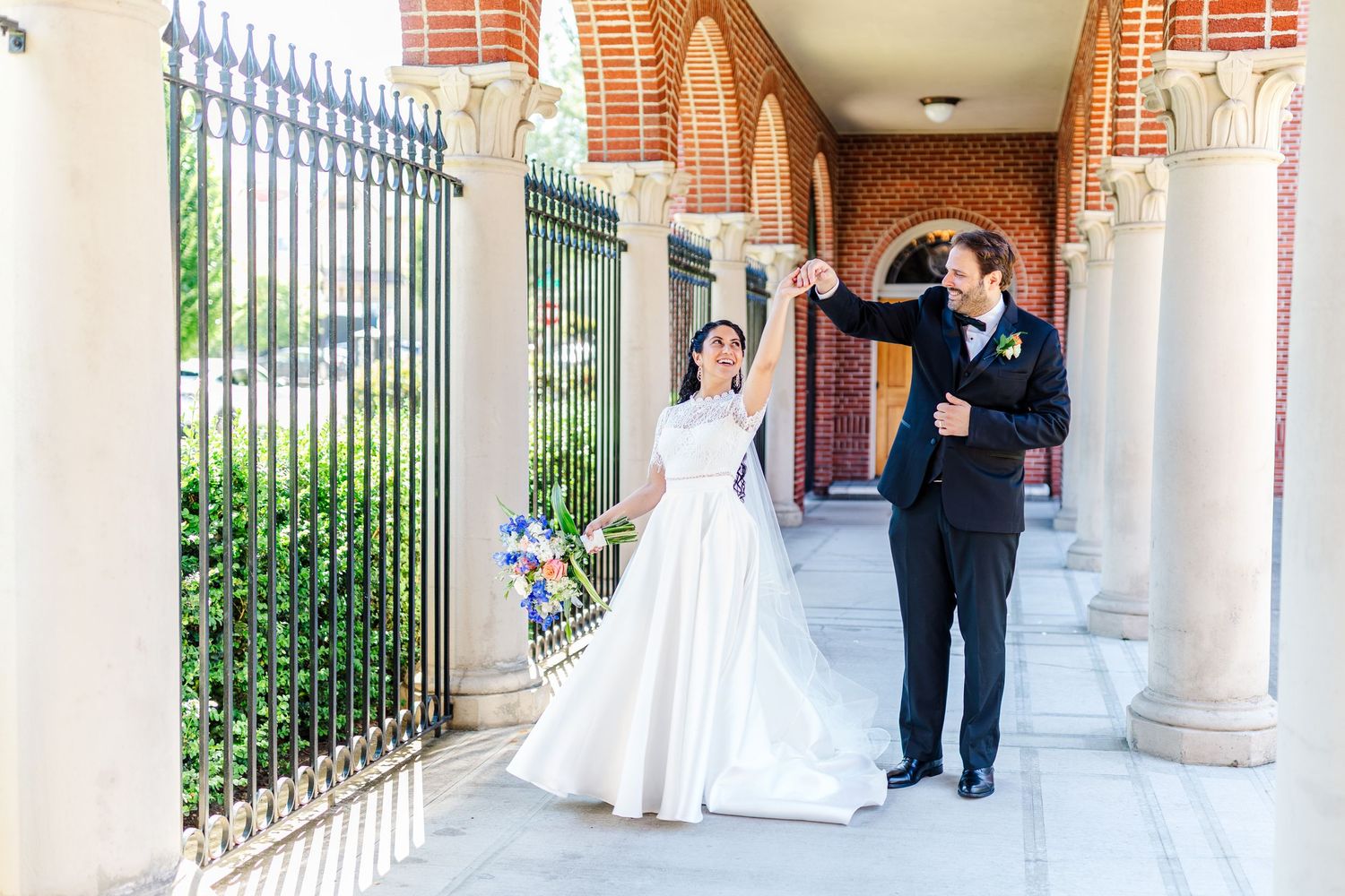 Couple walking and laughing together in an arched colonnade with white columns.