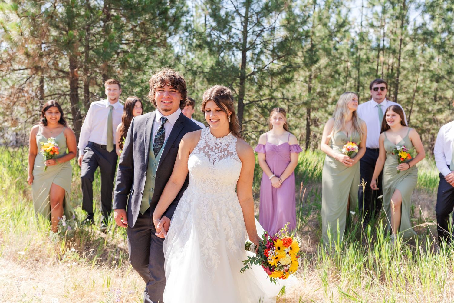 Wedding party poses in sunlit pine forest with bride in white dress.