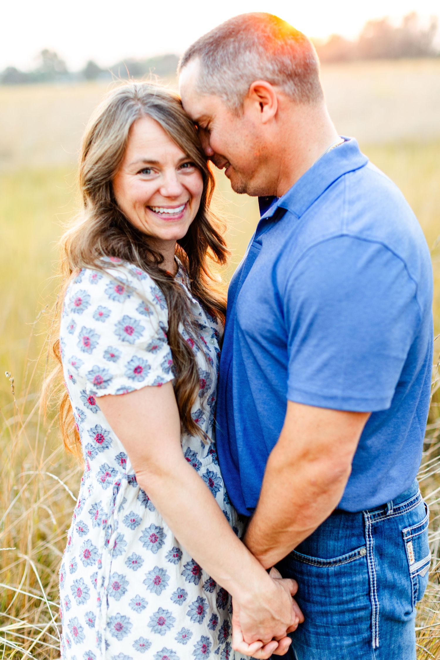 Romantic couple embraces in golden sunlit field during sunset photoshoot.