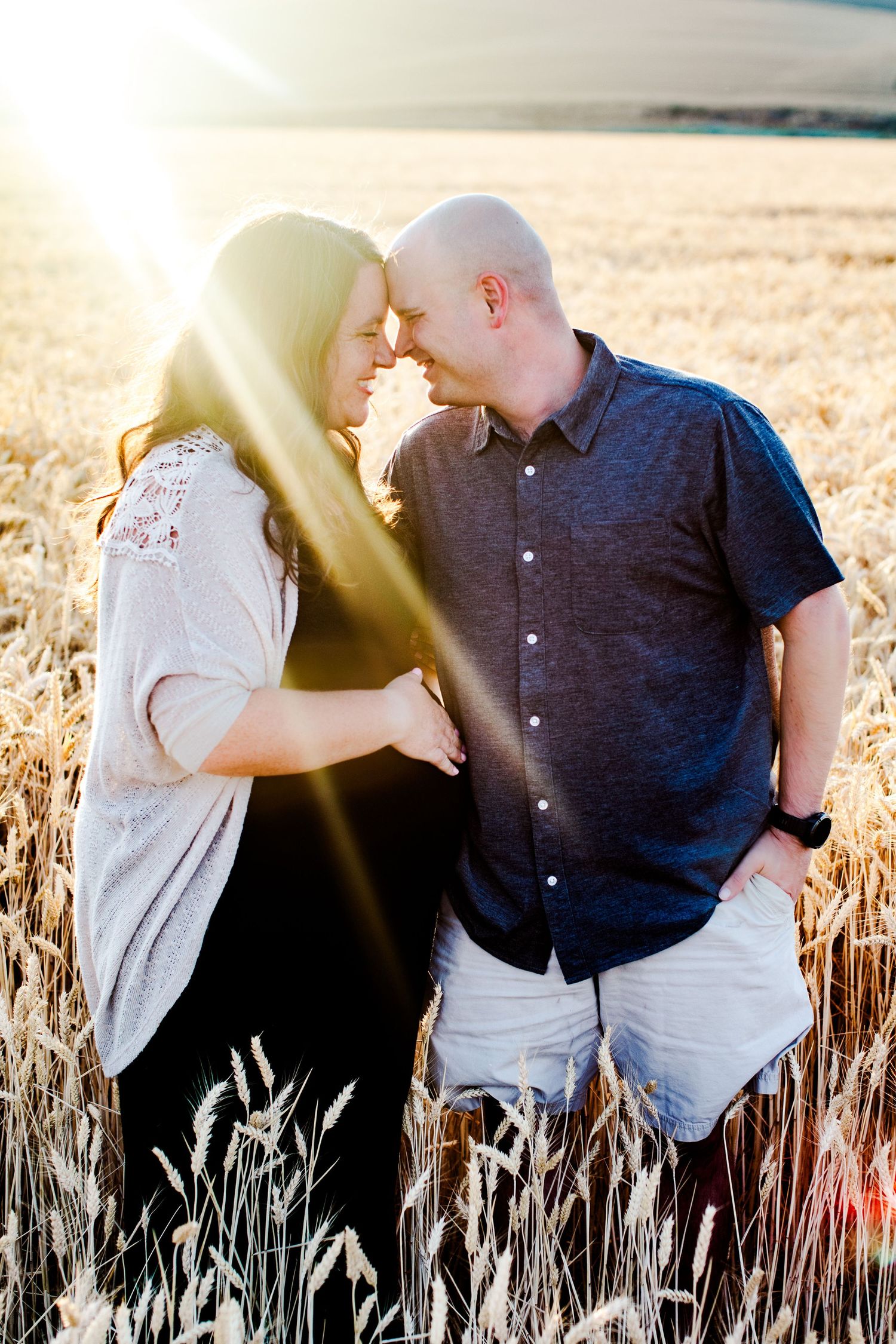 Romantic couple sharing intimate moment in sunlit wheat field.