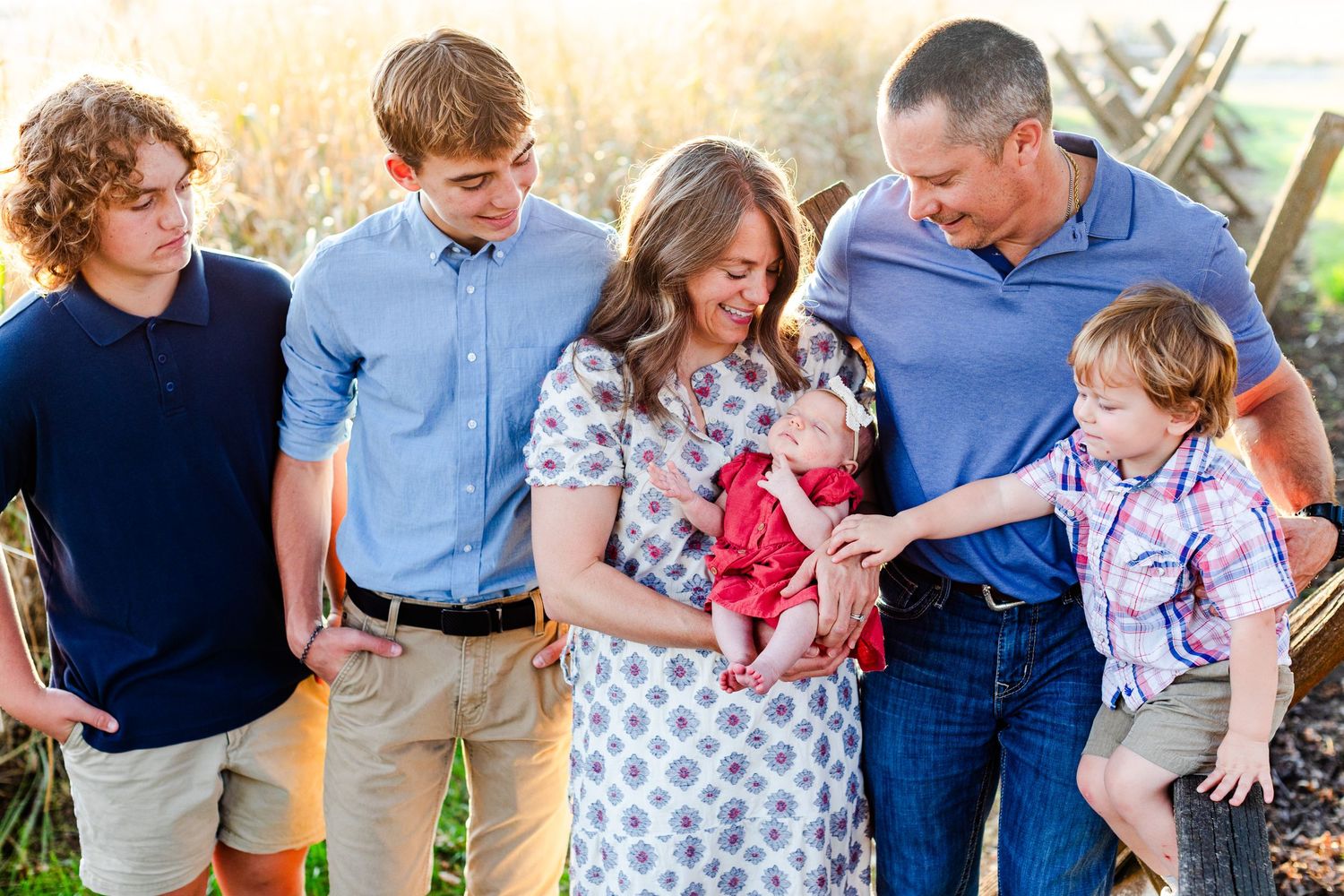 Family portrait in casual attire standing together in tall grass during golden hour.
