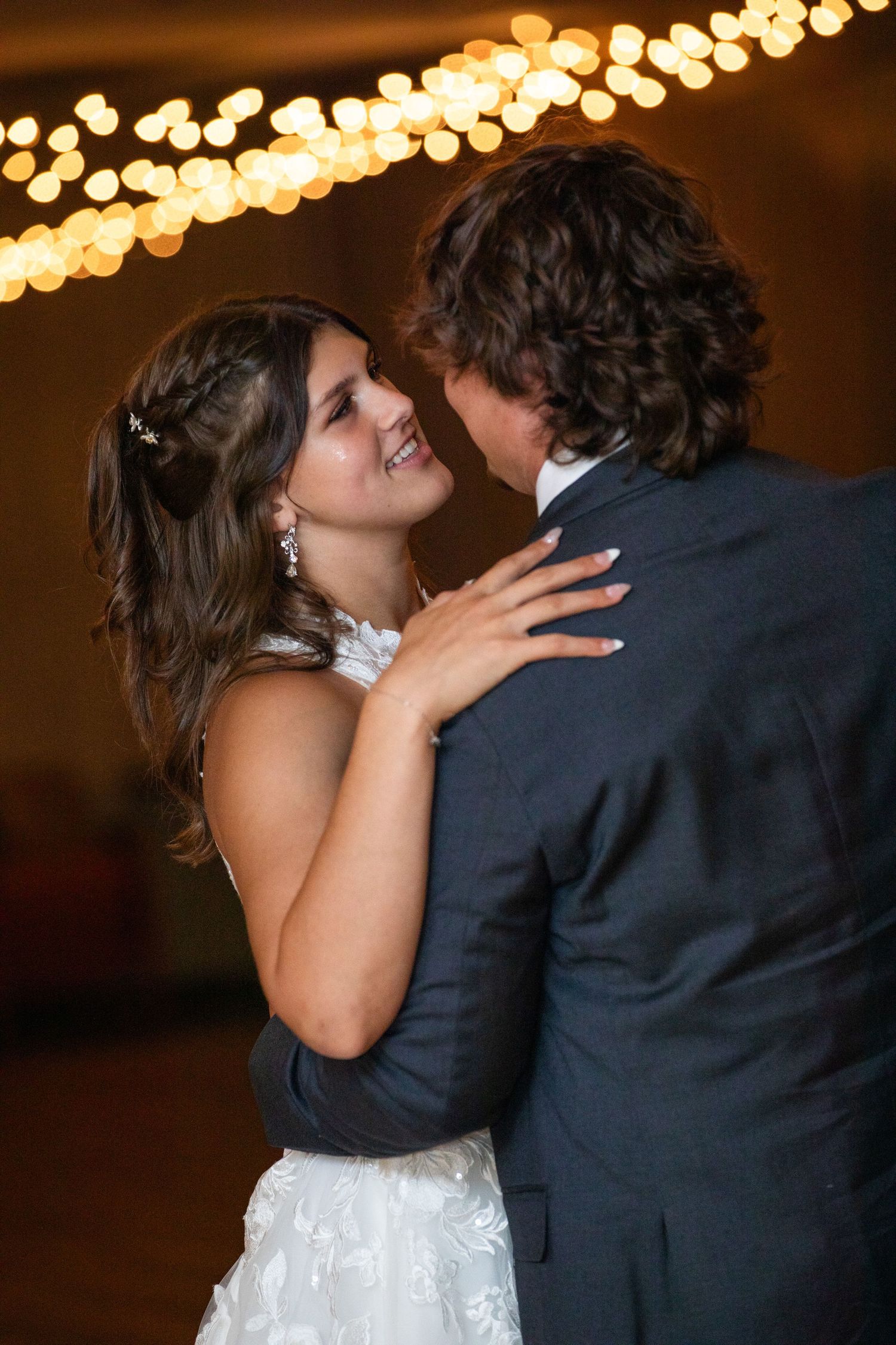 Romantic dance moment under warm string lights at wedding reception.