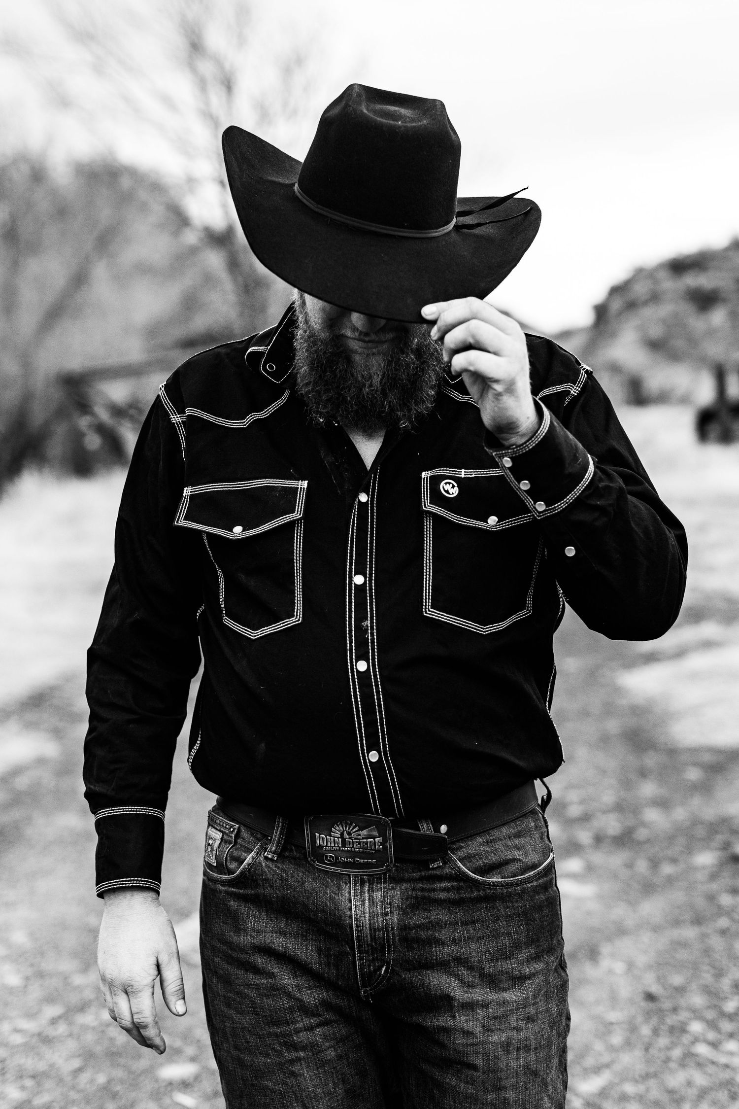 Person wearing western style black denim jacket and cowboy hat poses against rocky backdrop.