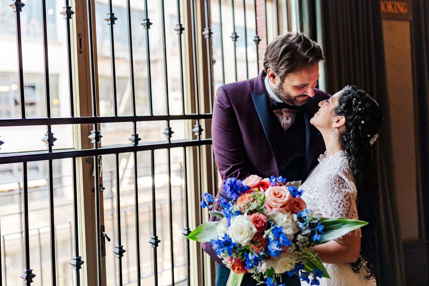 Romantic wedding portrait with colorful bouquet against iron window bars.