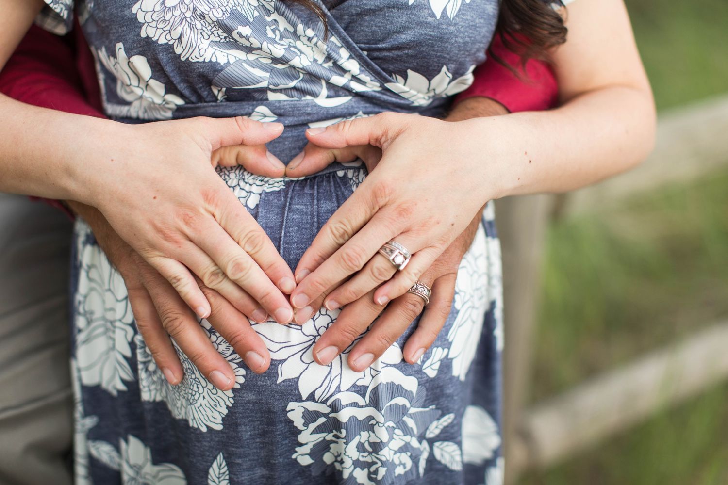 Woman wearing floral dress showing engagement ring outdoors.