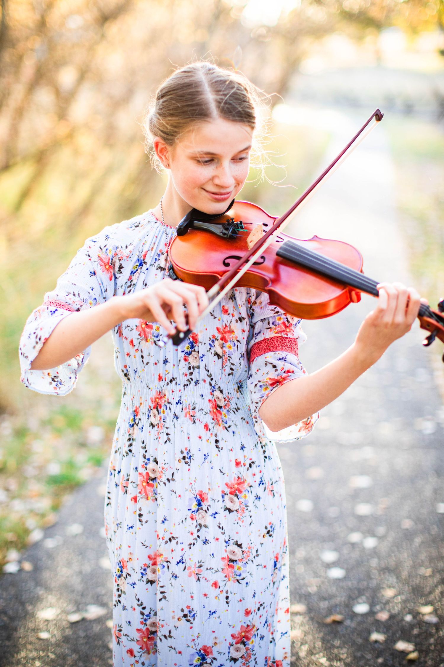 Girl in floral dress plays violin outdoors during sunset photo session.