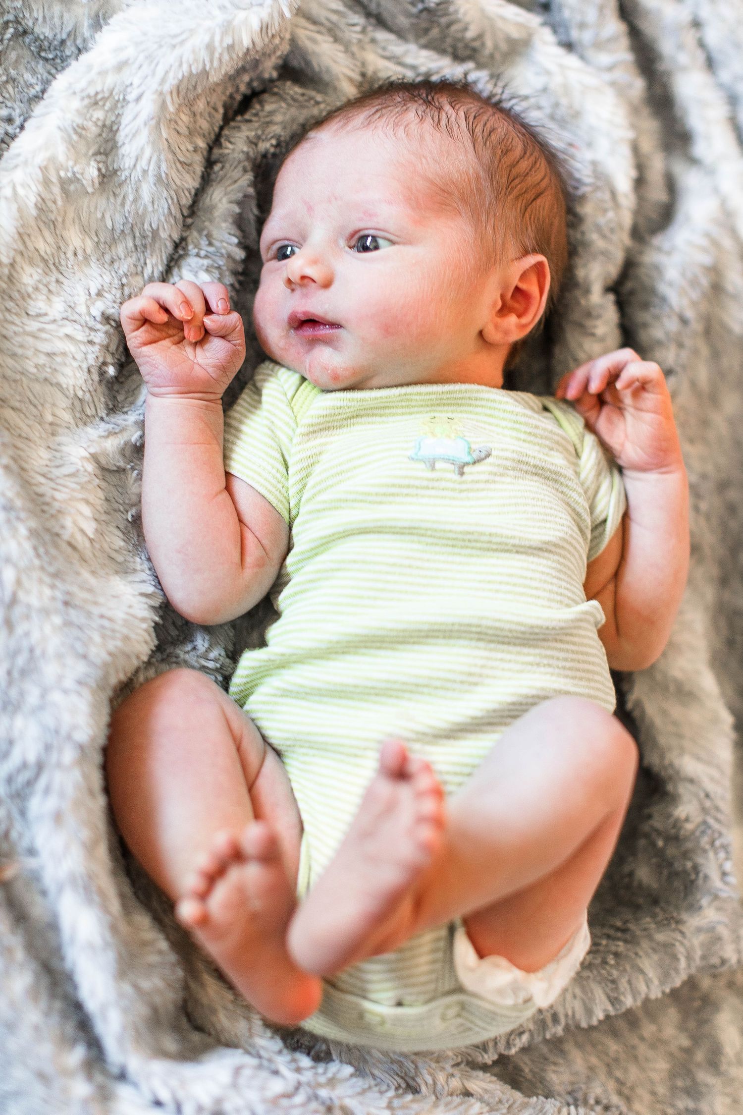 Baby wearing yellow striped onesie resting on plush grey blanket.