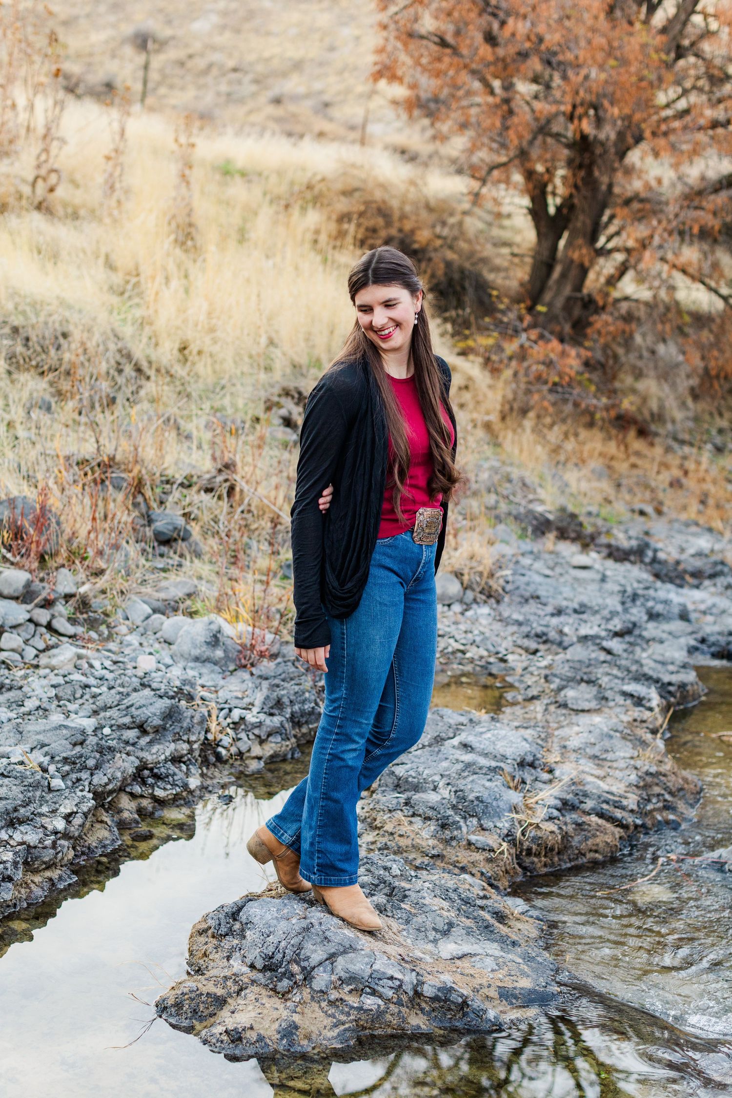 Person in casual wear exploring rocky creek bed with autumn foliage in background.