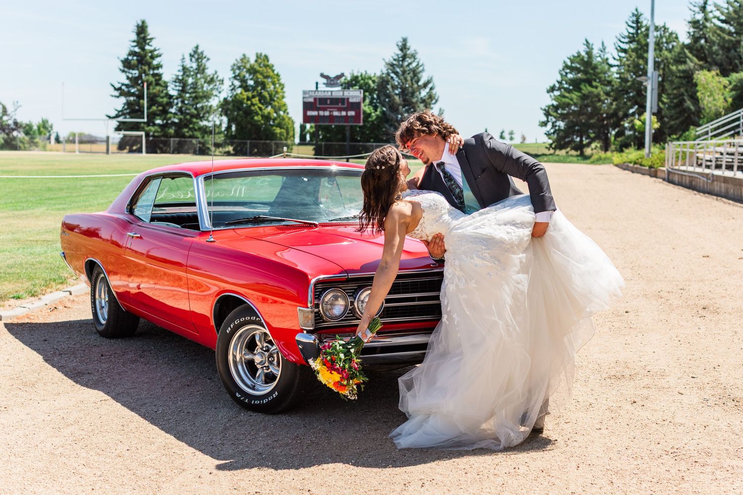 Wedding couple poses with a classic red vintage car outdoors.