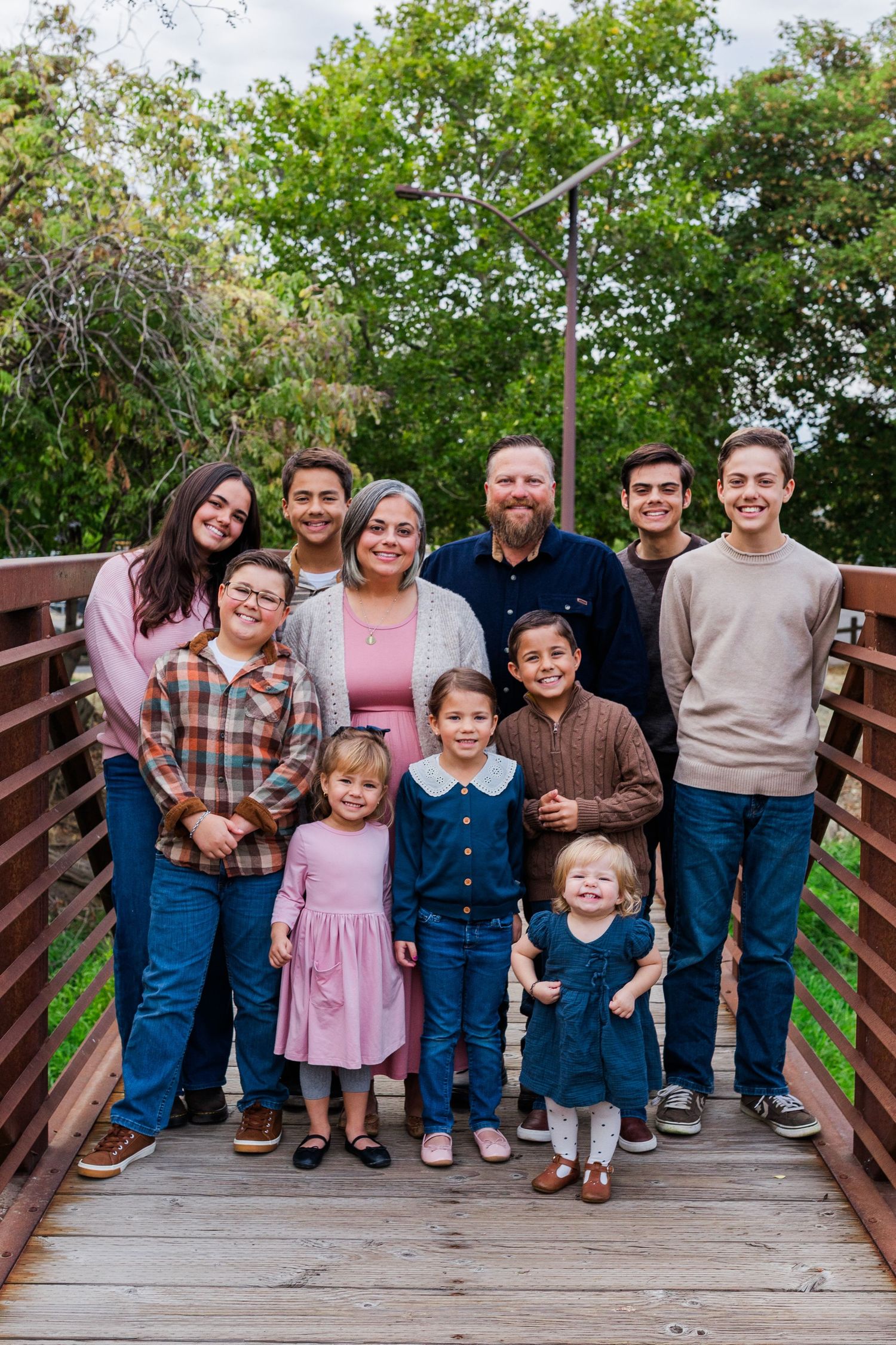 Family group poses together on a wooden bridge surrounded by green trees.