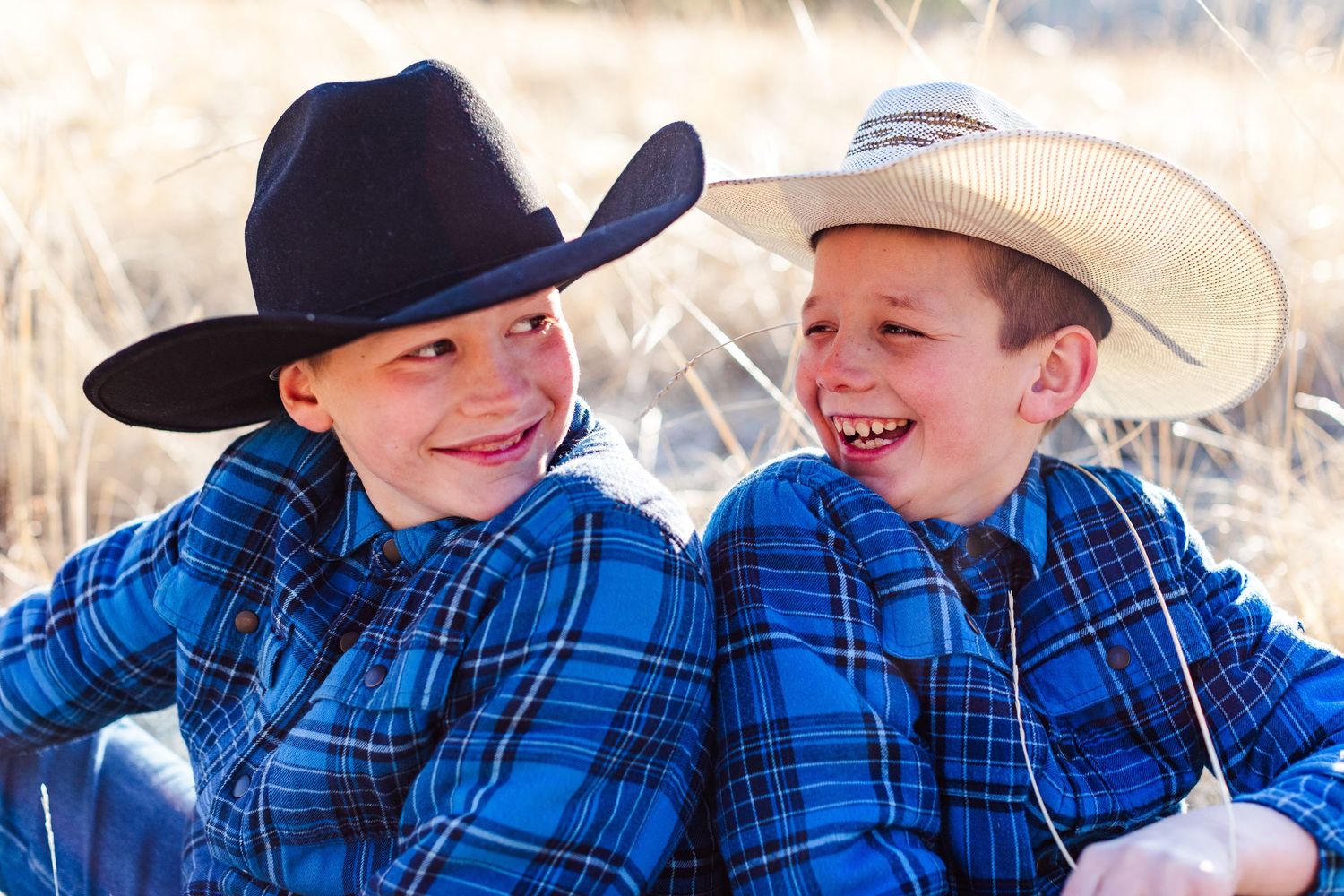 Two children in western wear share laughs while practicing their roping skills outdoors.