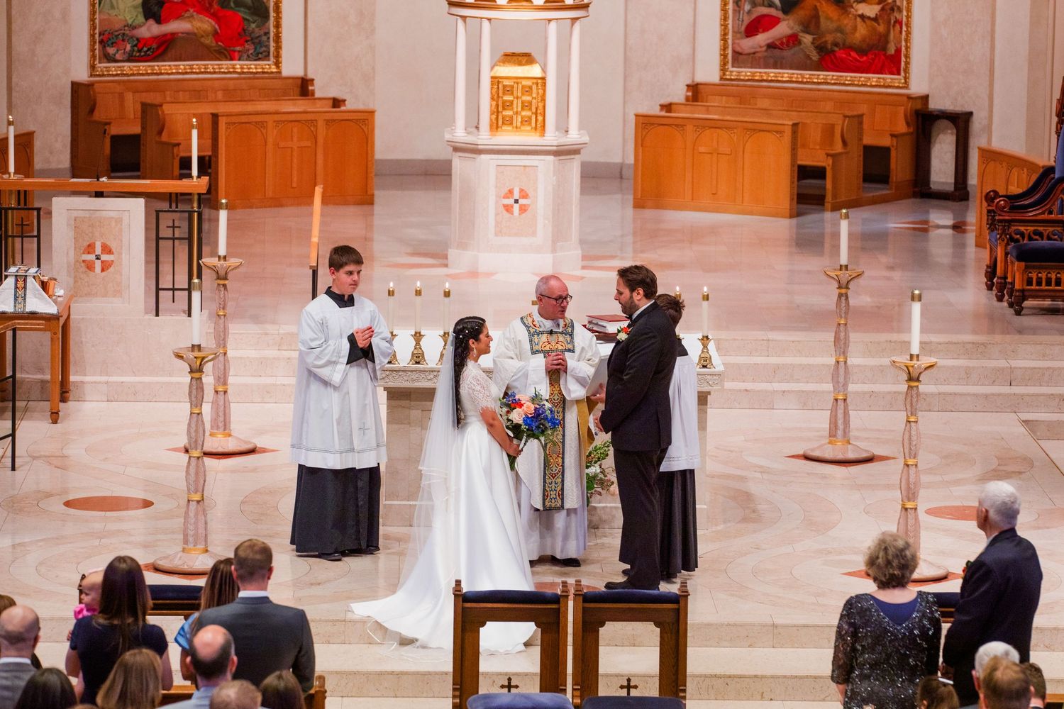 Religious ceremony taking place in a grand cathedral interior with priests and attendees gathered near the altar.