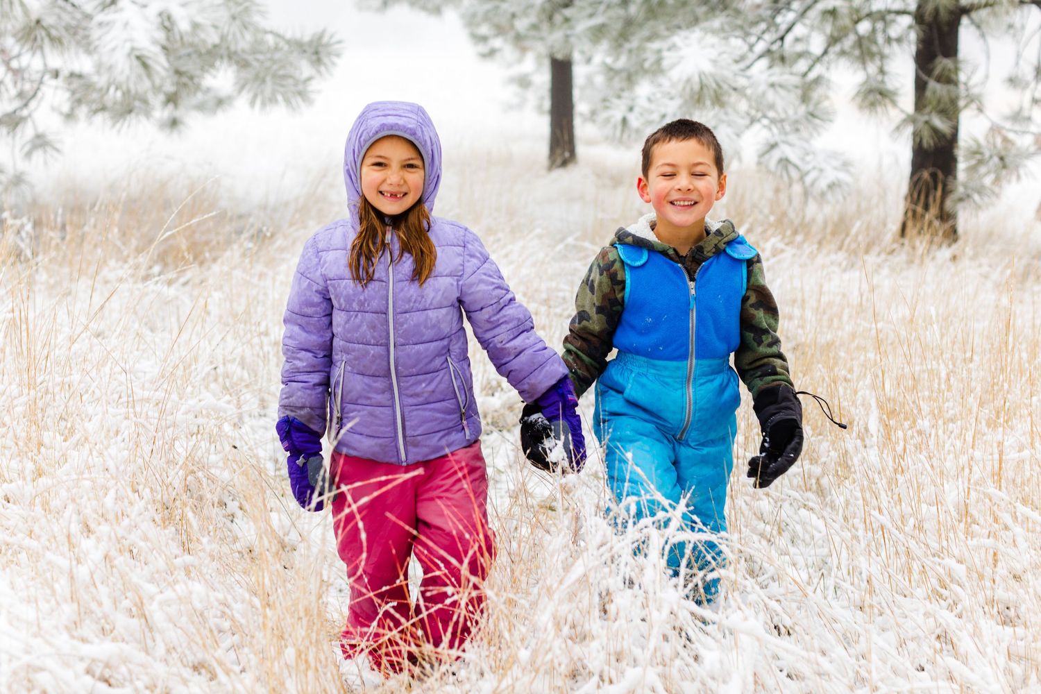 Children playing and laughing in the snow wearing bright winter coats.