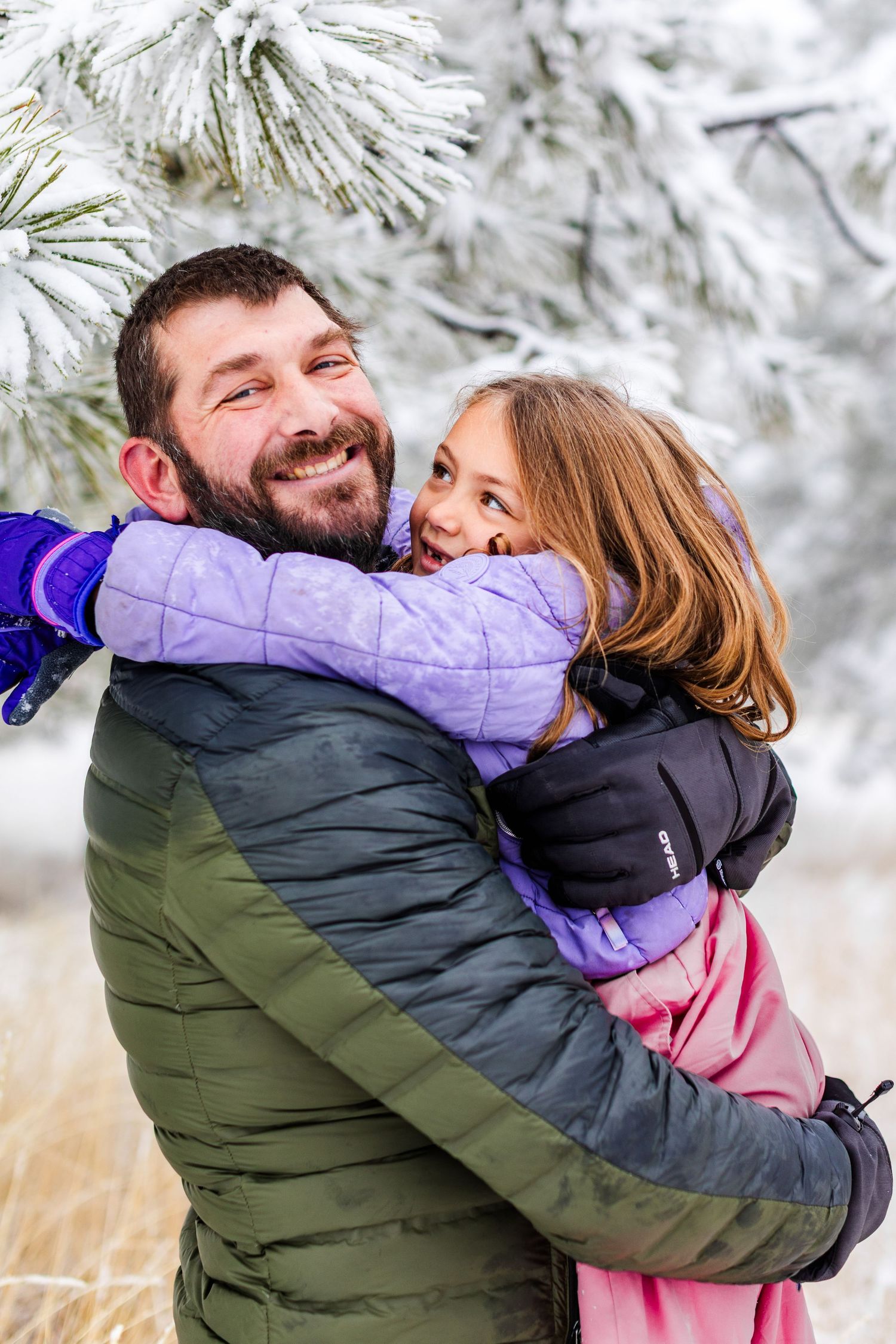 Playful winter scene with people embracing and laughing in puffy coats among snow-covered trees.