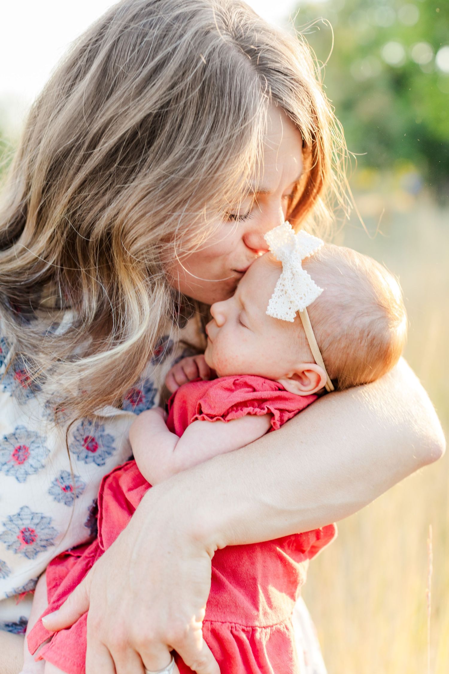 Tender moment between parent and baby in sunlit outdoor setting.