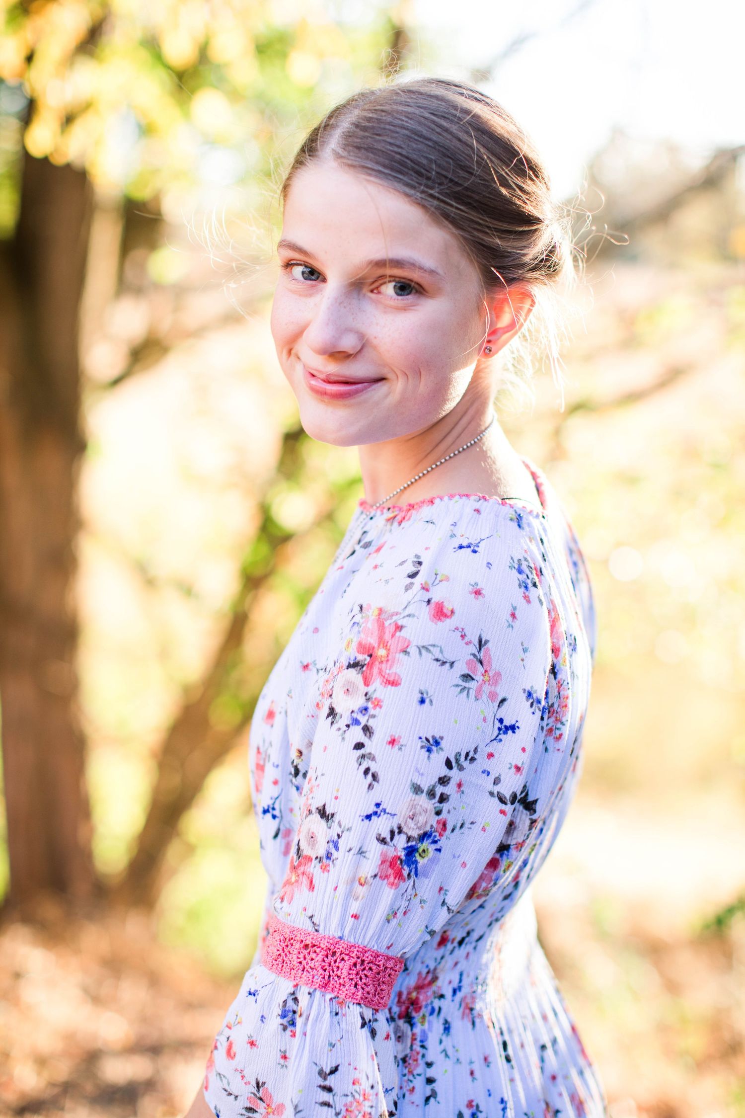 Young girl in floral dress poses outdoors during golden hour portrait session.
