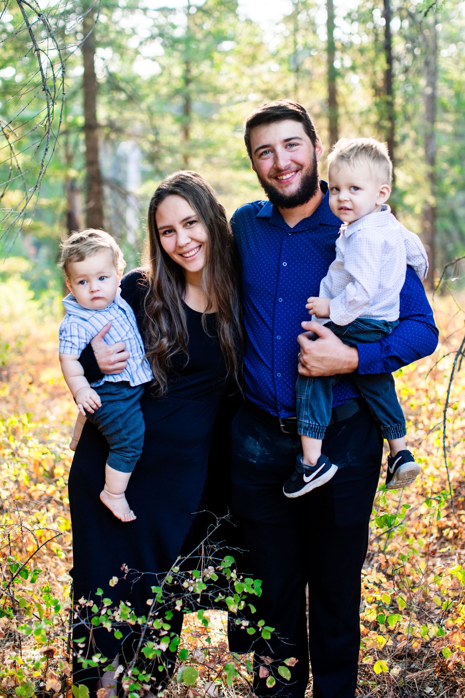 Family of three posing together in wooded area during fall season.