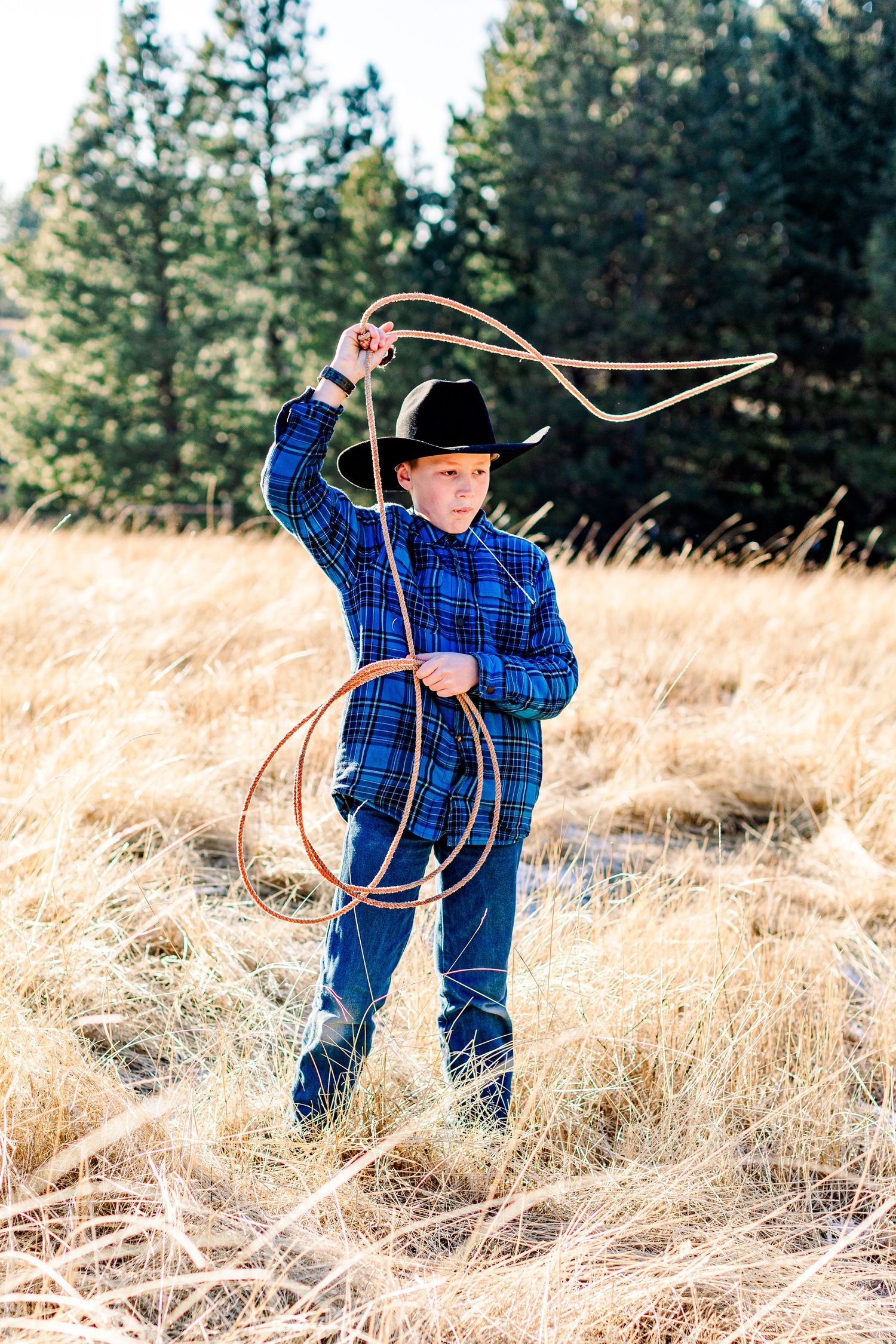 Young cowboys in matching blue plaid shirts practice lasso roping techniques in a golden wheat field.