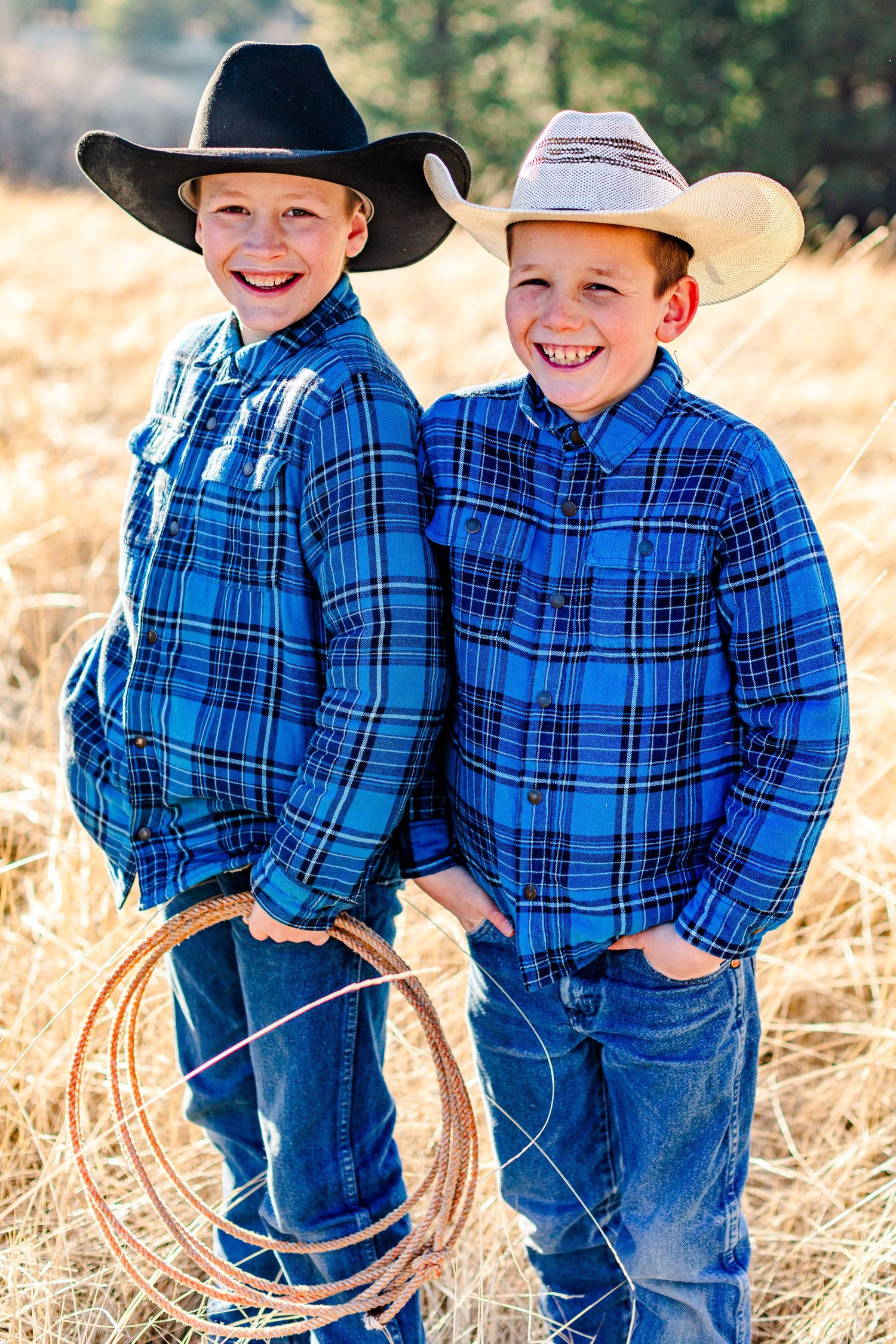 Cowboys in matching blue plaid shirts and jeans stand together holding lassos in a sunny field.