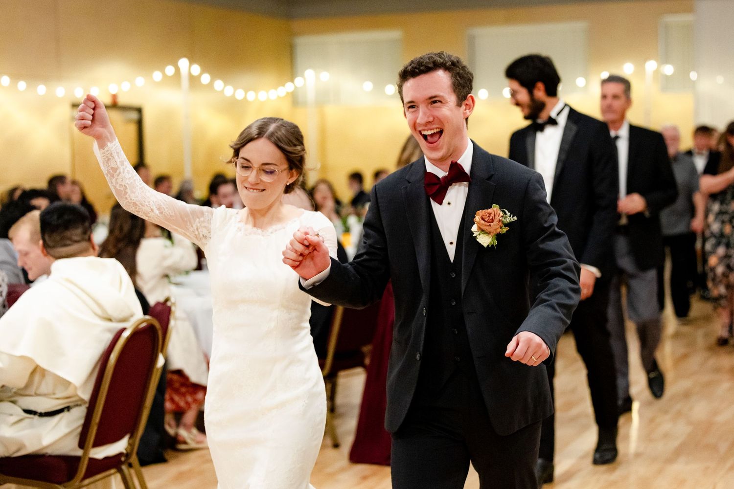 Joyful wedding reception dancing with guests celebrating on dance floor under string lights.