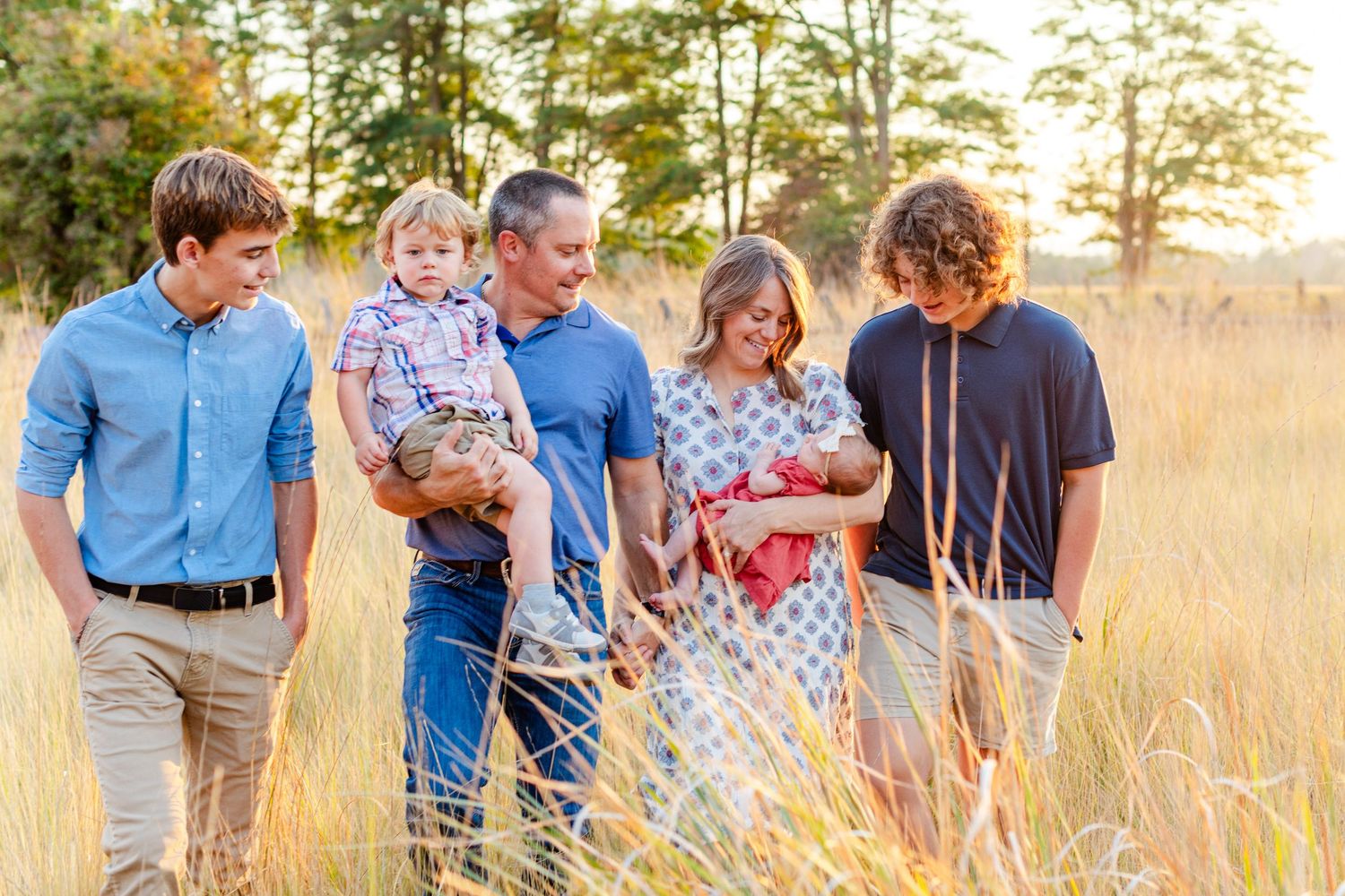 Family of five walking through tall grass field at golden hour.
