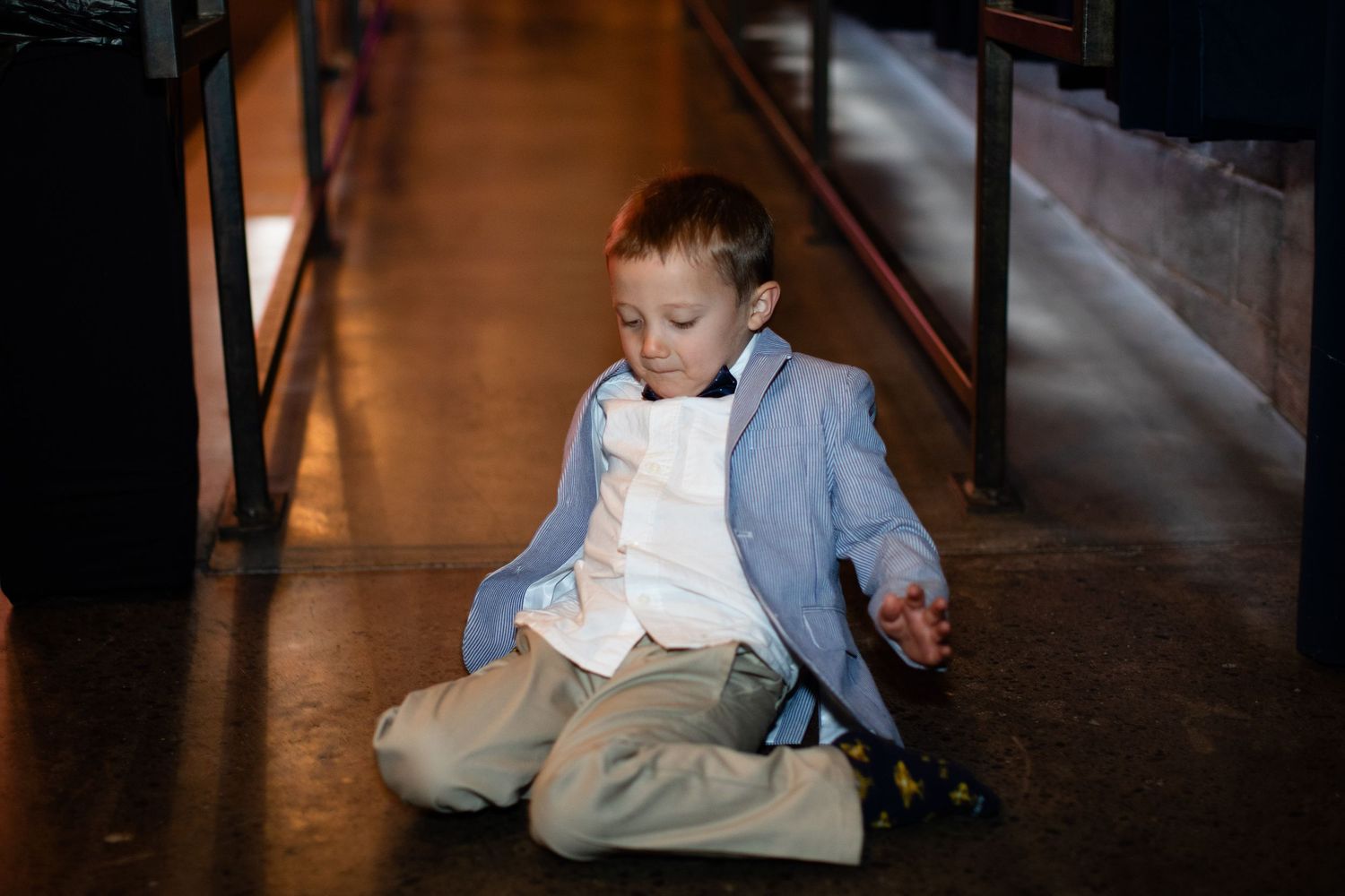 Young boy in blue blazer and khakis sitting on floor, looking down at something in his hands.