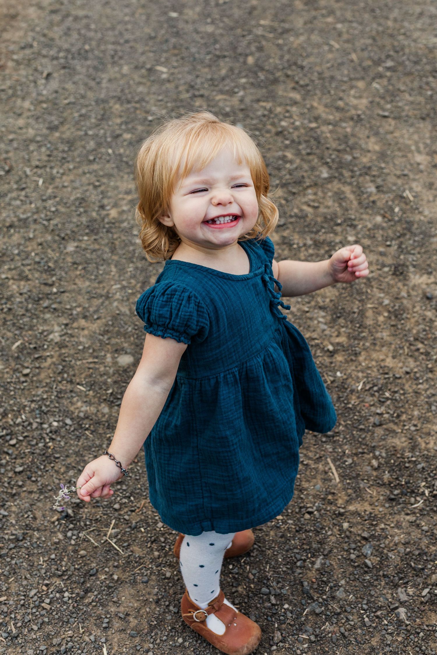 Toddler in navy blue dress twirls and plays on rocky ground.