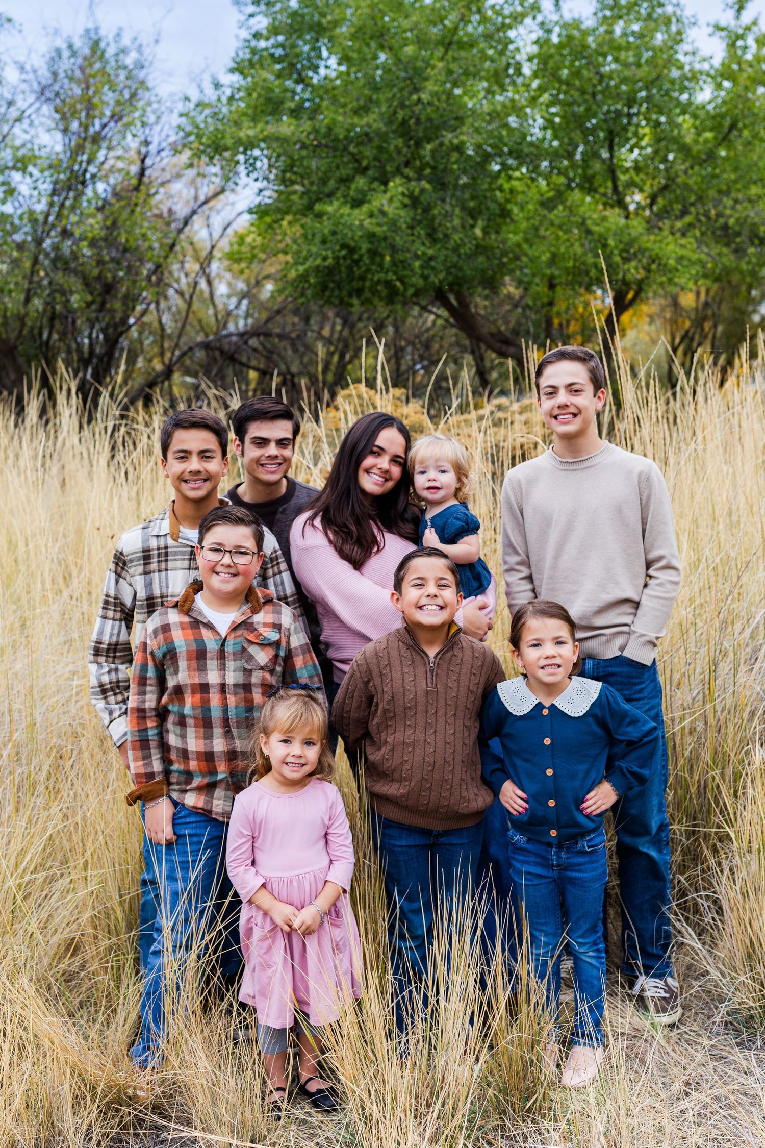 Family group portrait in tall golden grass with trees in background.