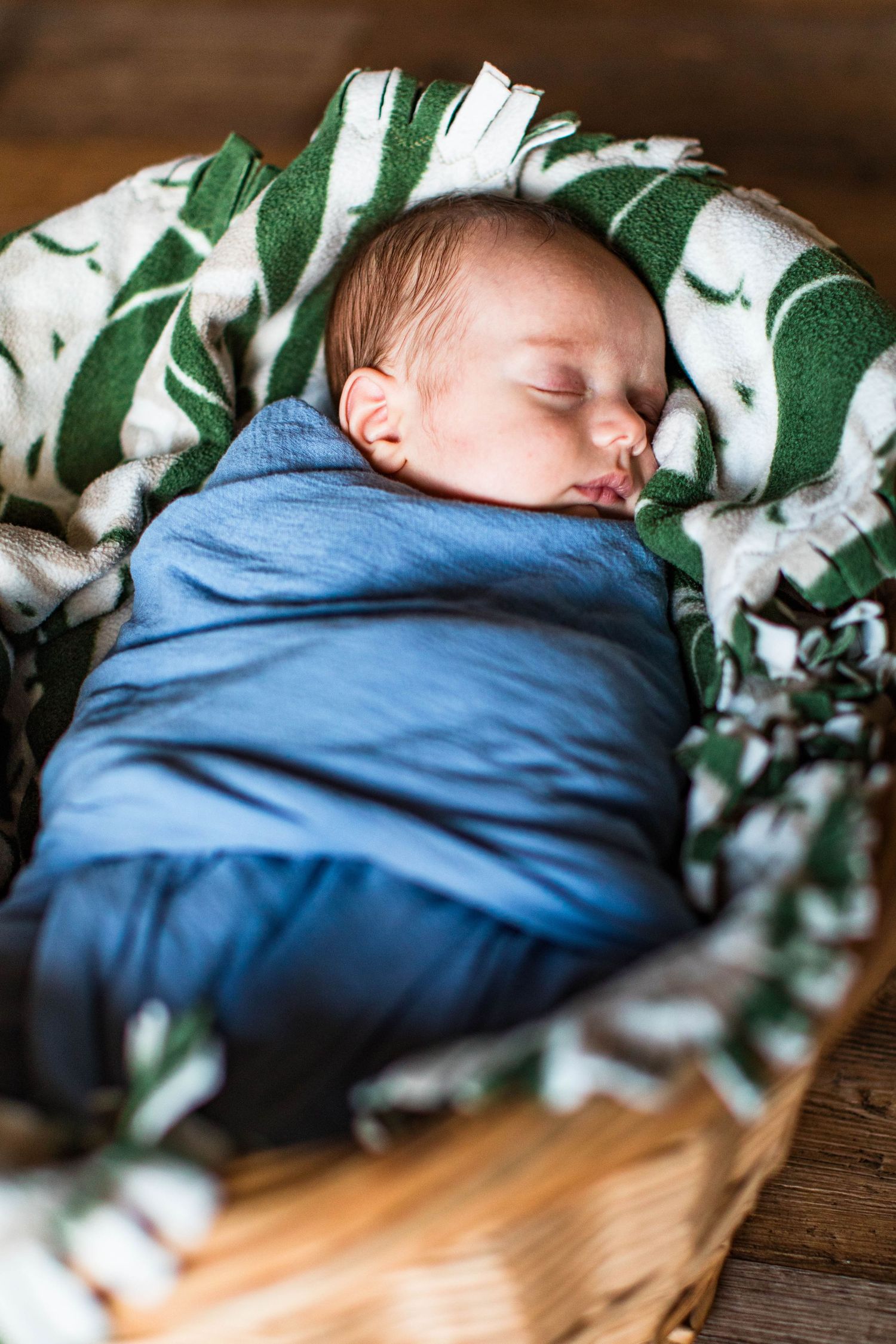 Sleeping newborn wrapped in blue swaddle with botanical print backdrop.
