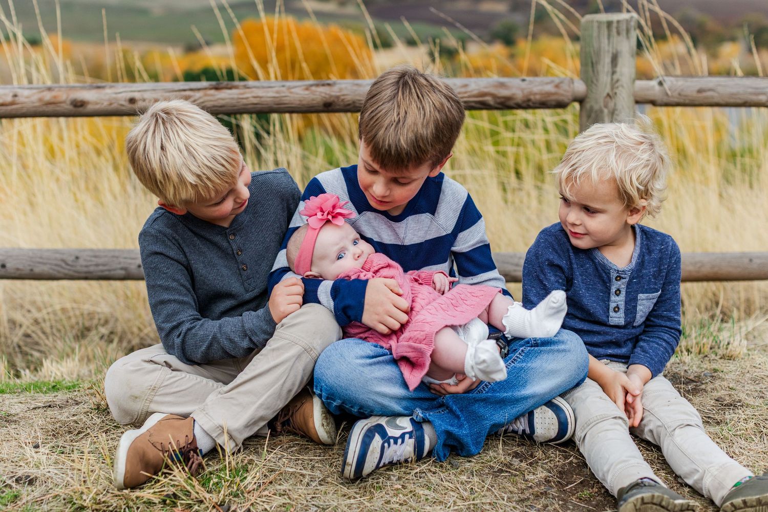 Children sit together in tall grass during an outdoor family photo session.