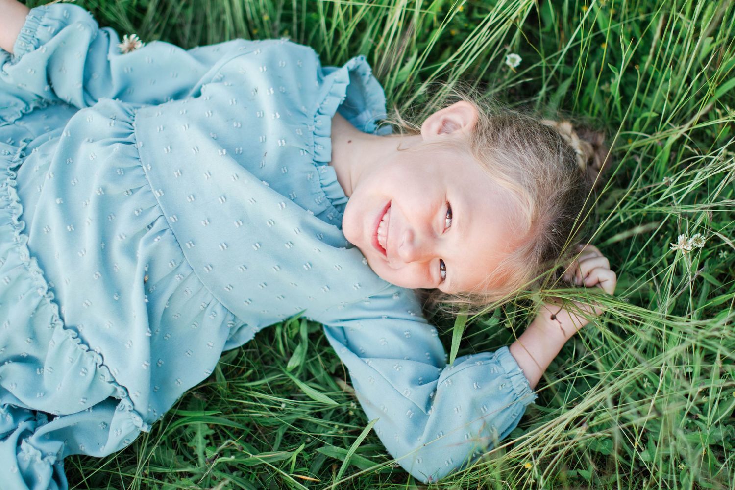 Artistic portrait series of someone lying in tall grass wearing light blue clothing.