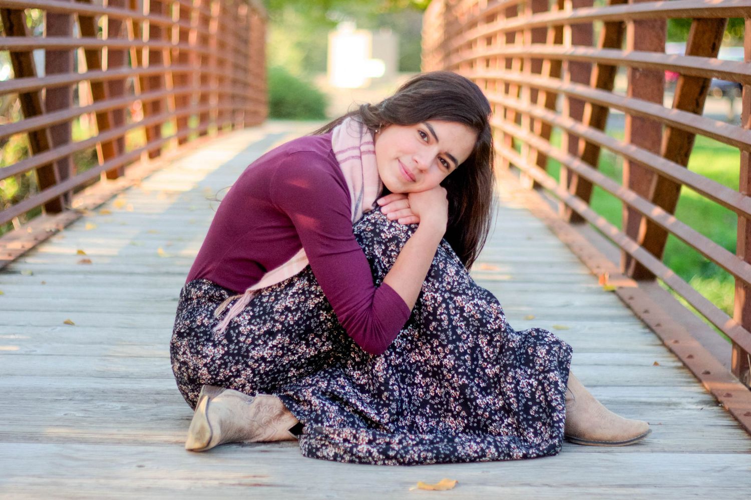 Woman in floral dress posing on wooden bridge during sunset photoshoot.